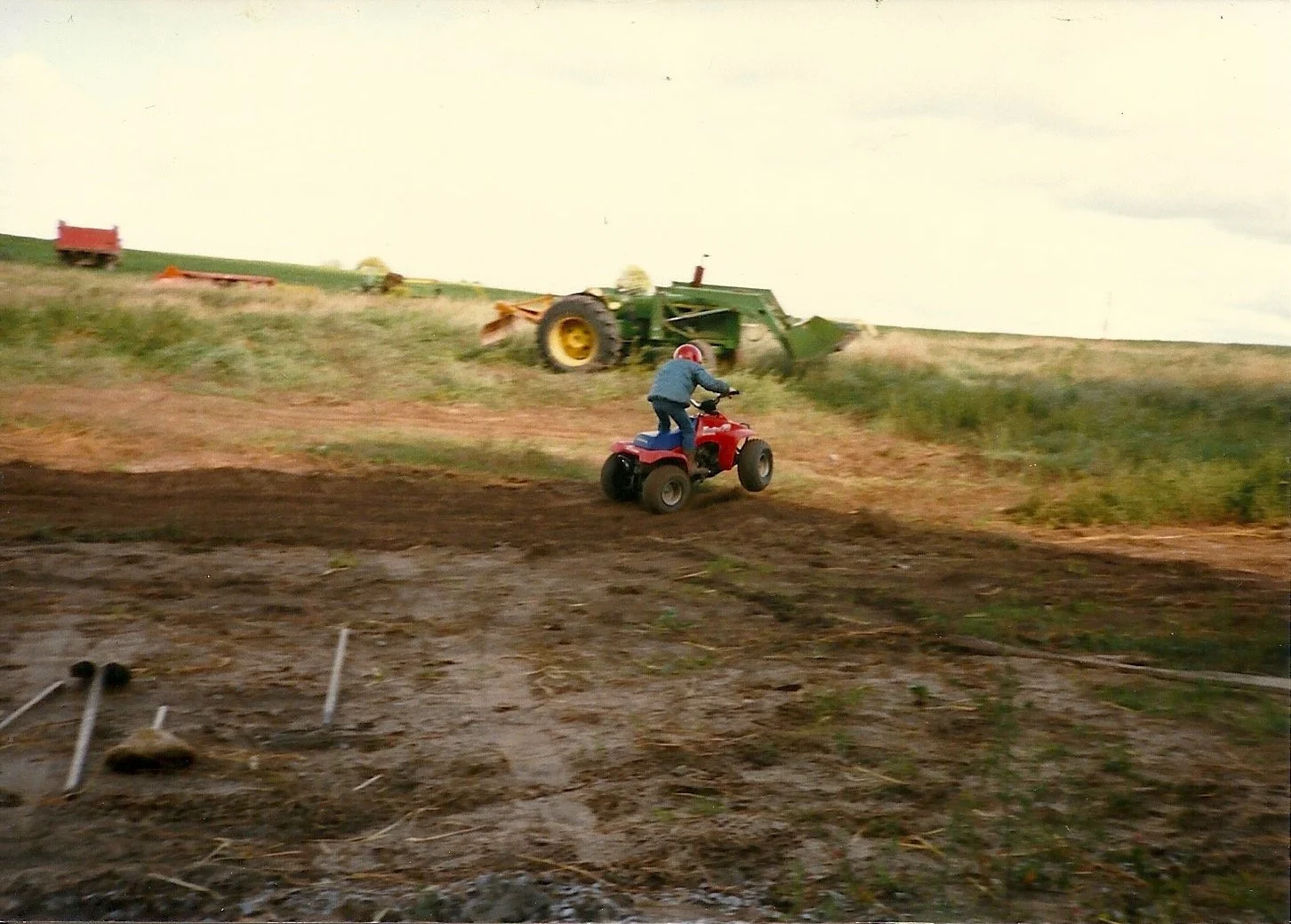 Kid riding a four wheel motorcycle in front of a tractor