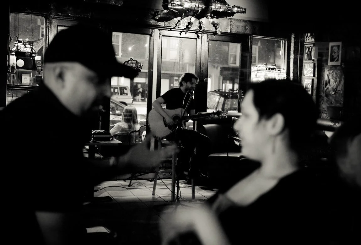 Man playing guitar with two people talking in foreground