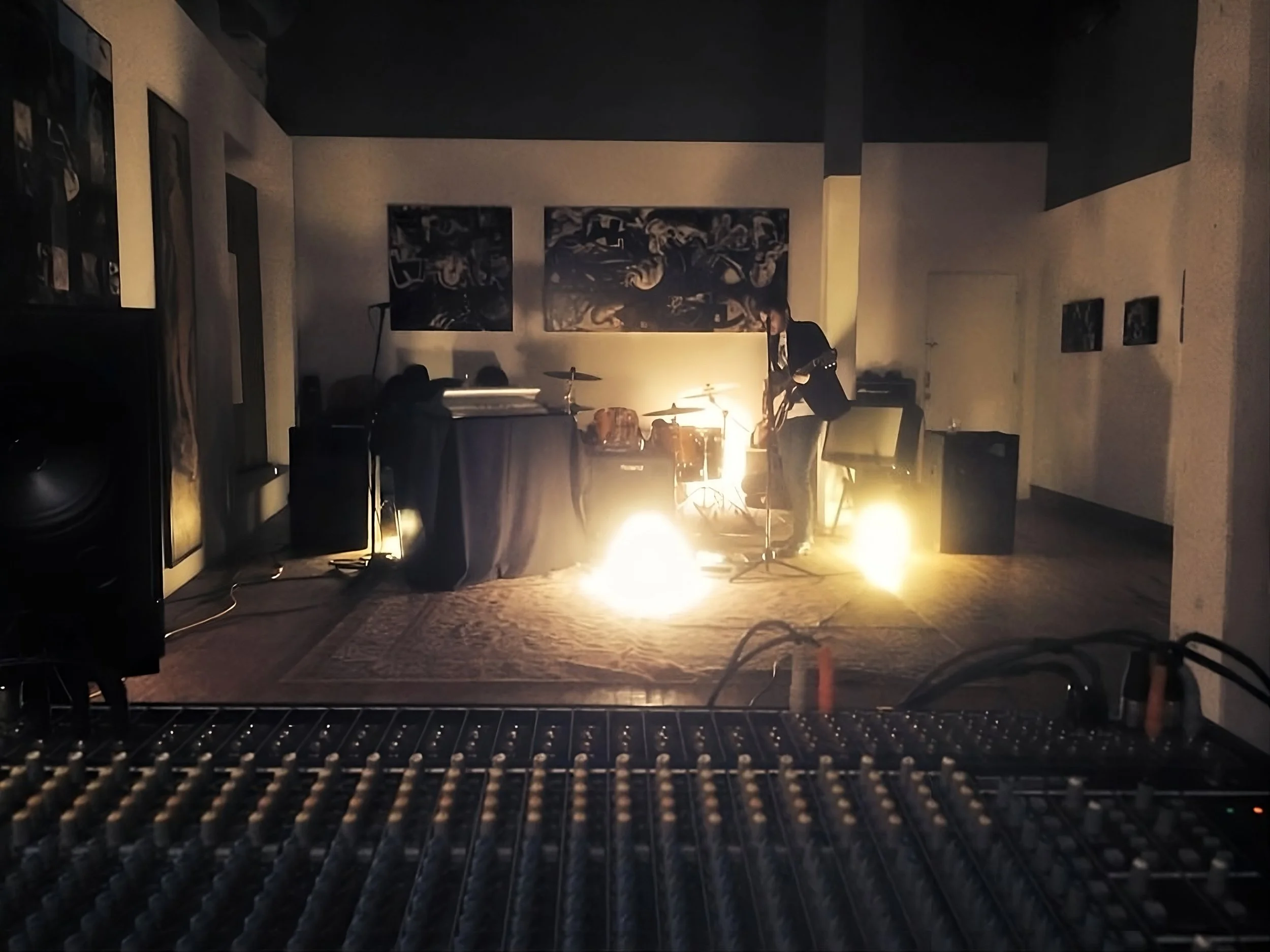 Man with guitar standing in lights in front of an audio sound board
