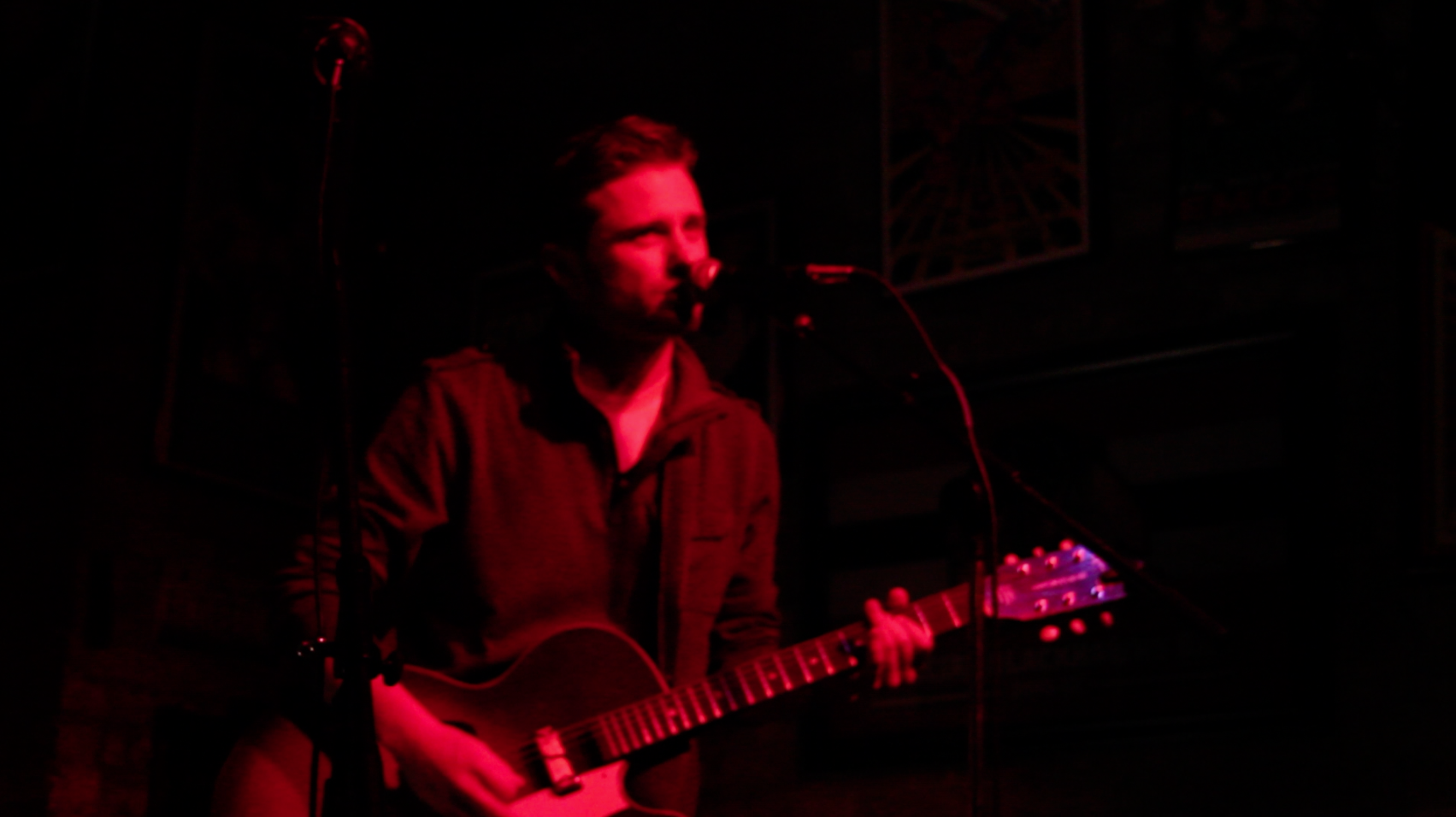 Man performing guitar under red lights