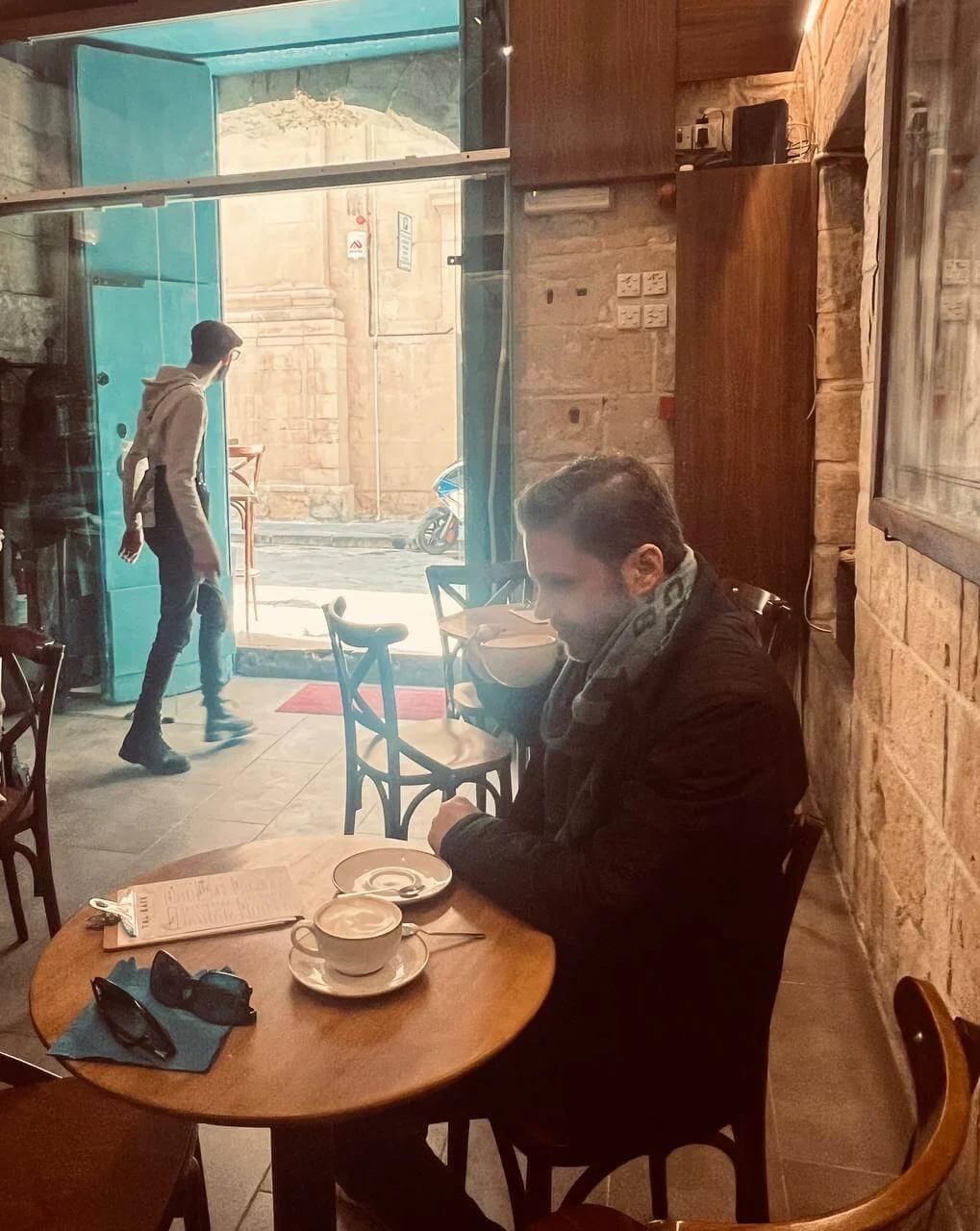 Man drinking coffee as barista looks out the door in Valletta, Malta