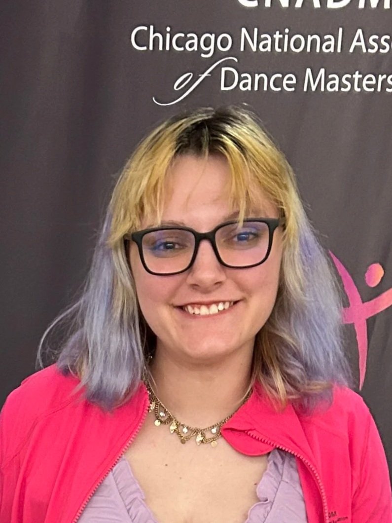 Scenic landscape of green rolling hills and mountains with snow-capped peaks in the background, featuring modern buildings nestled in the hills under a cloudy sky.