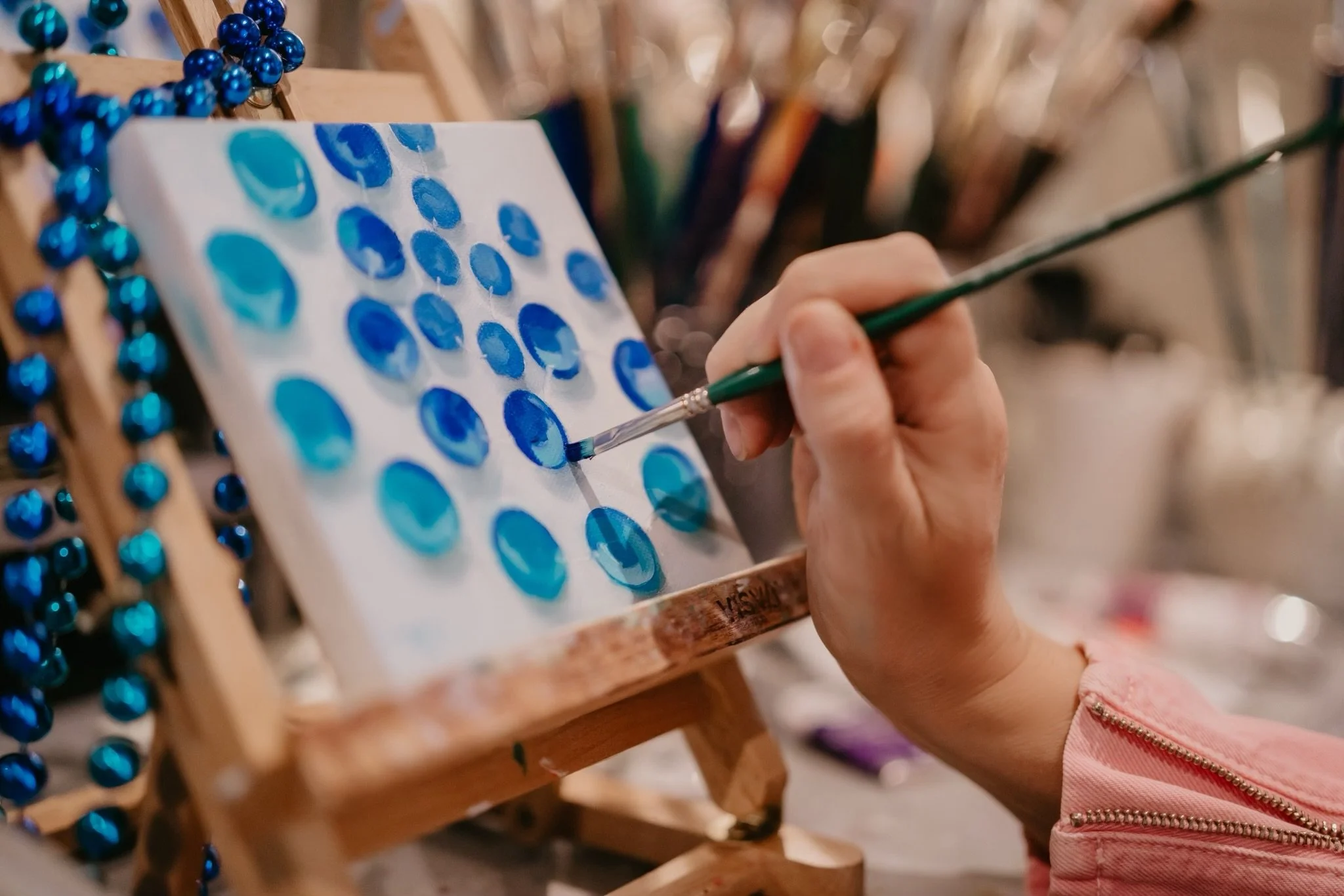 Someone painting blue circles on a white canvas with a small brush at an art studio.