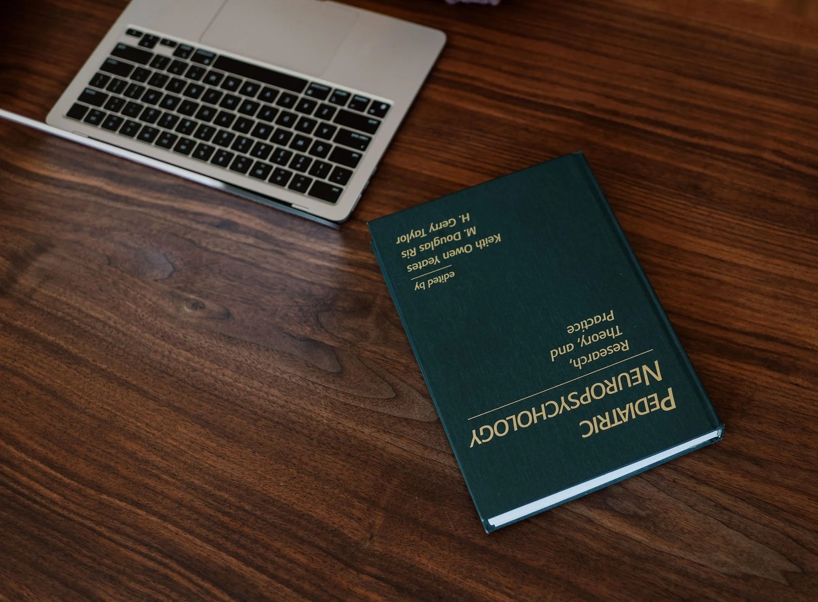 Laptop and pediatric neuropsychology book on wood table