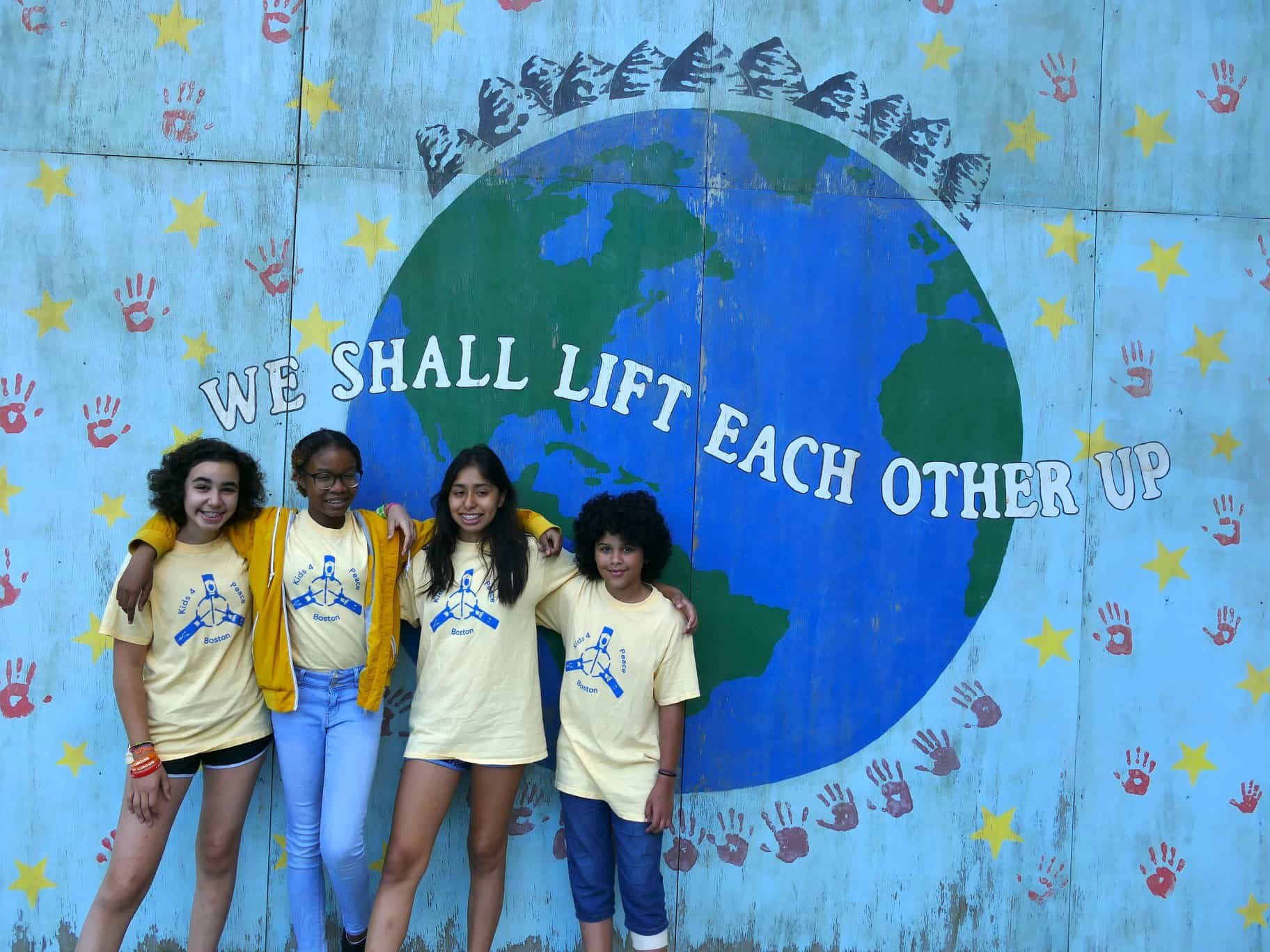 Youth pose in front of a mural stating "we shall lift each other"