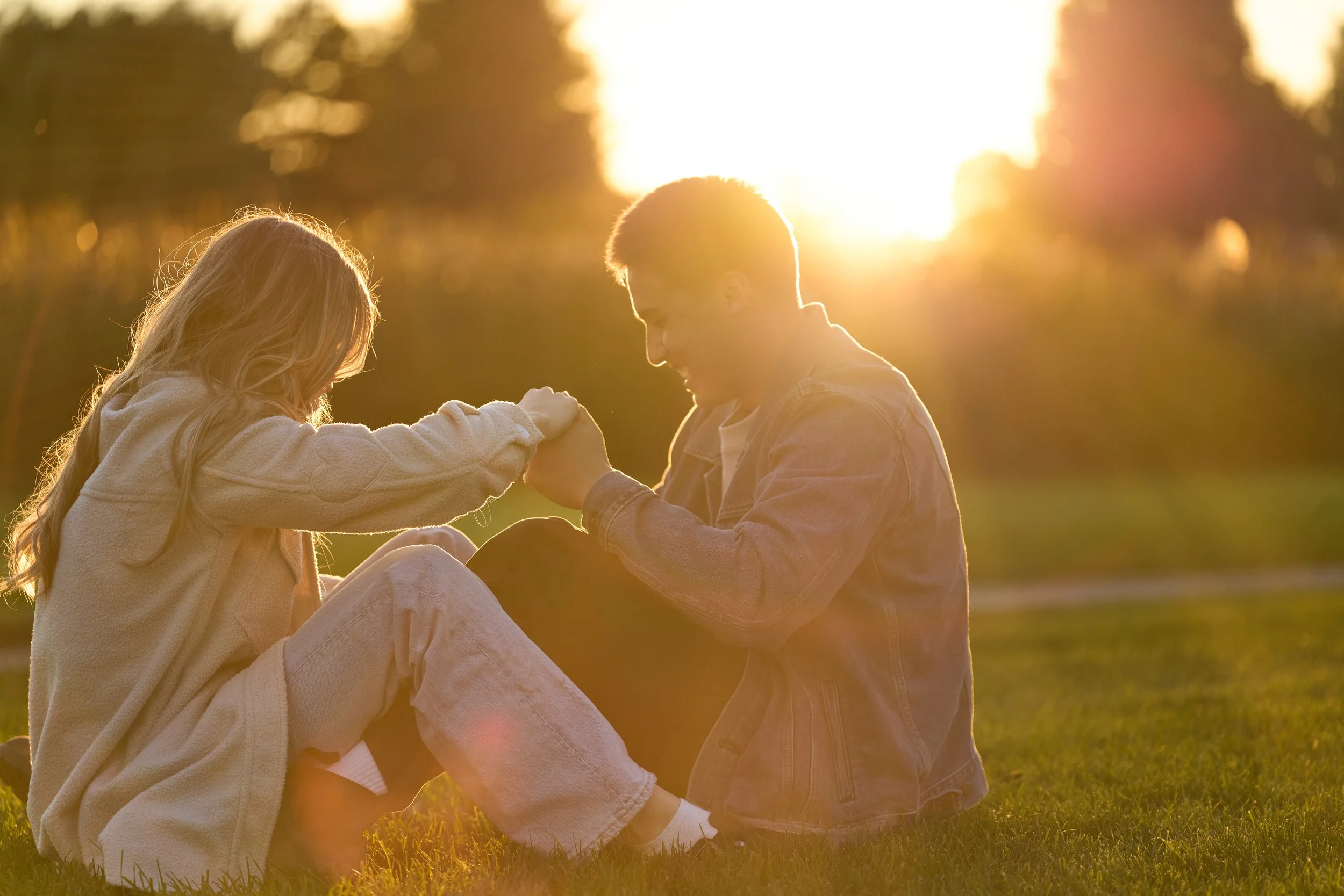 A couple sitting on grass, holding hands at sunset.