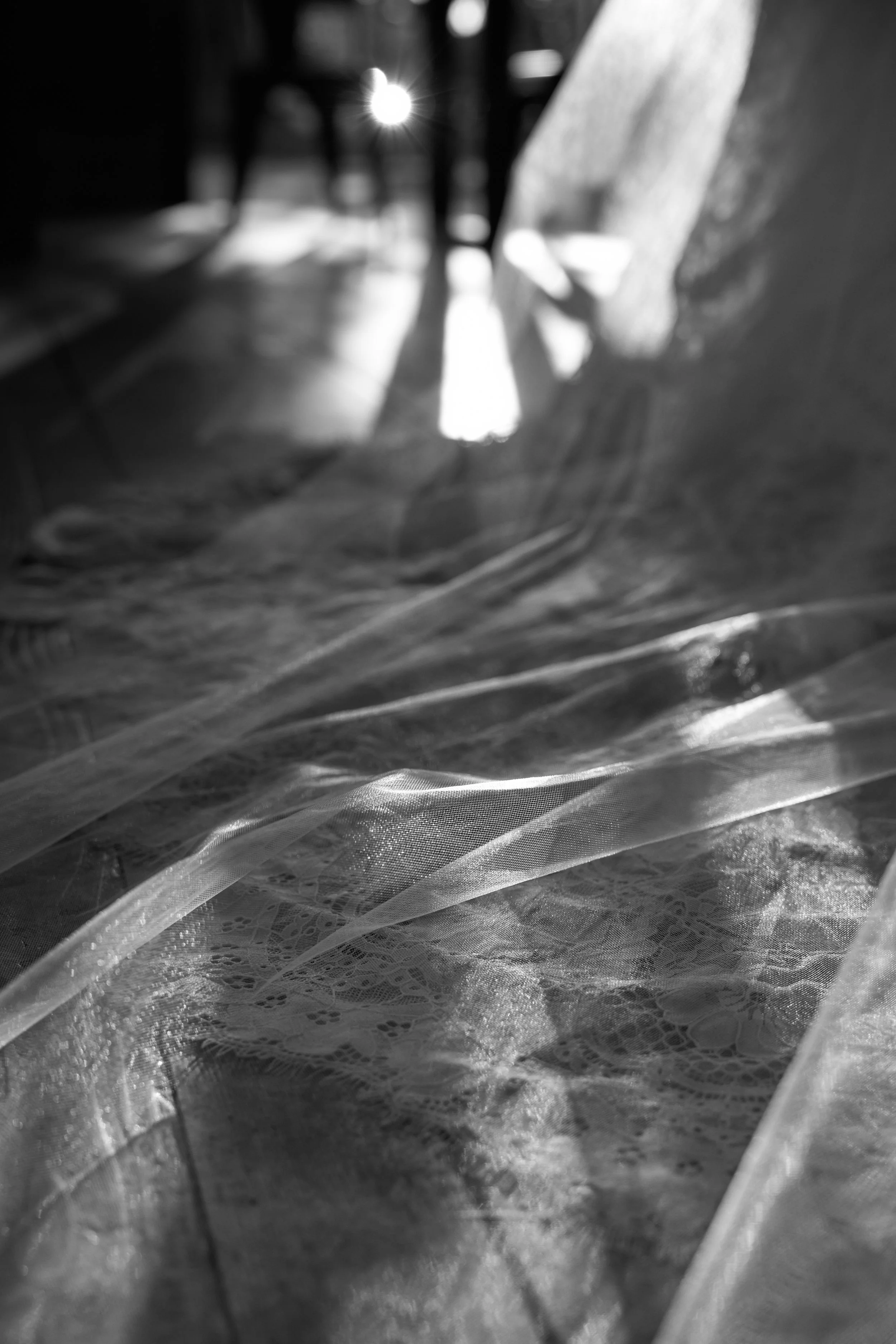 Black and white photo of sunlight streaming through fabric, creating shadows and patterns on a lace surface.
