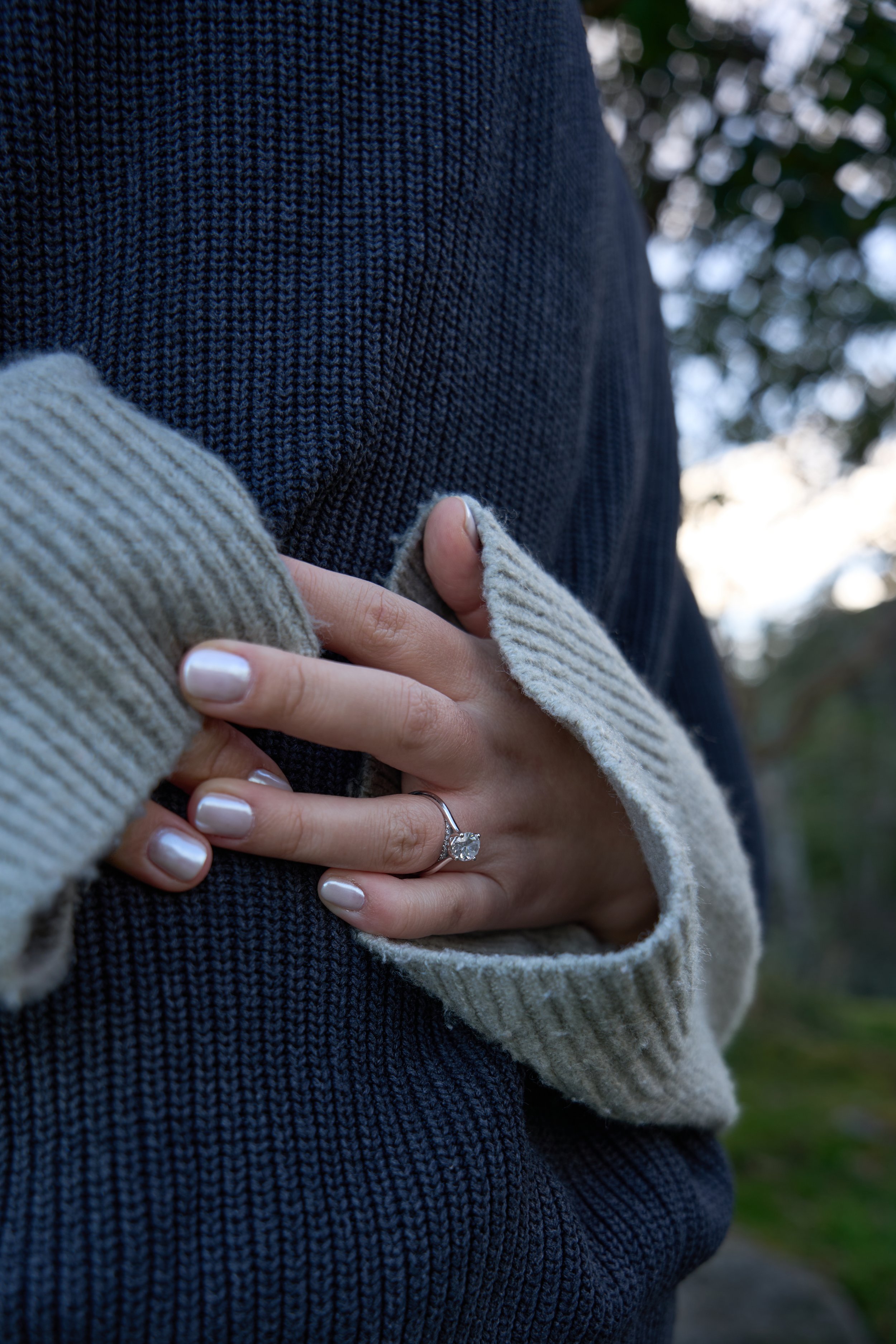 Close-up of a hand with a ring on finger, resting on a blue knit sweater with gray ribbed sleeves.