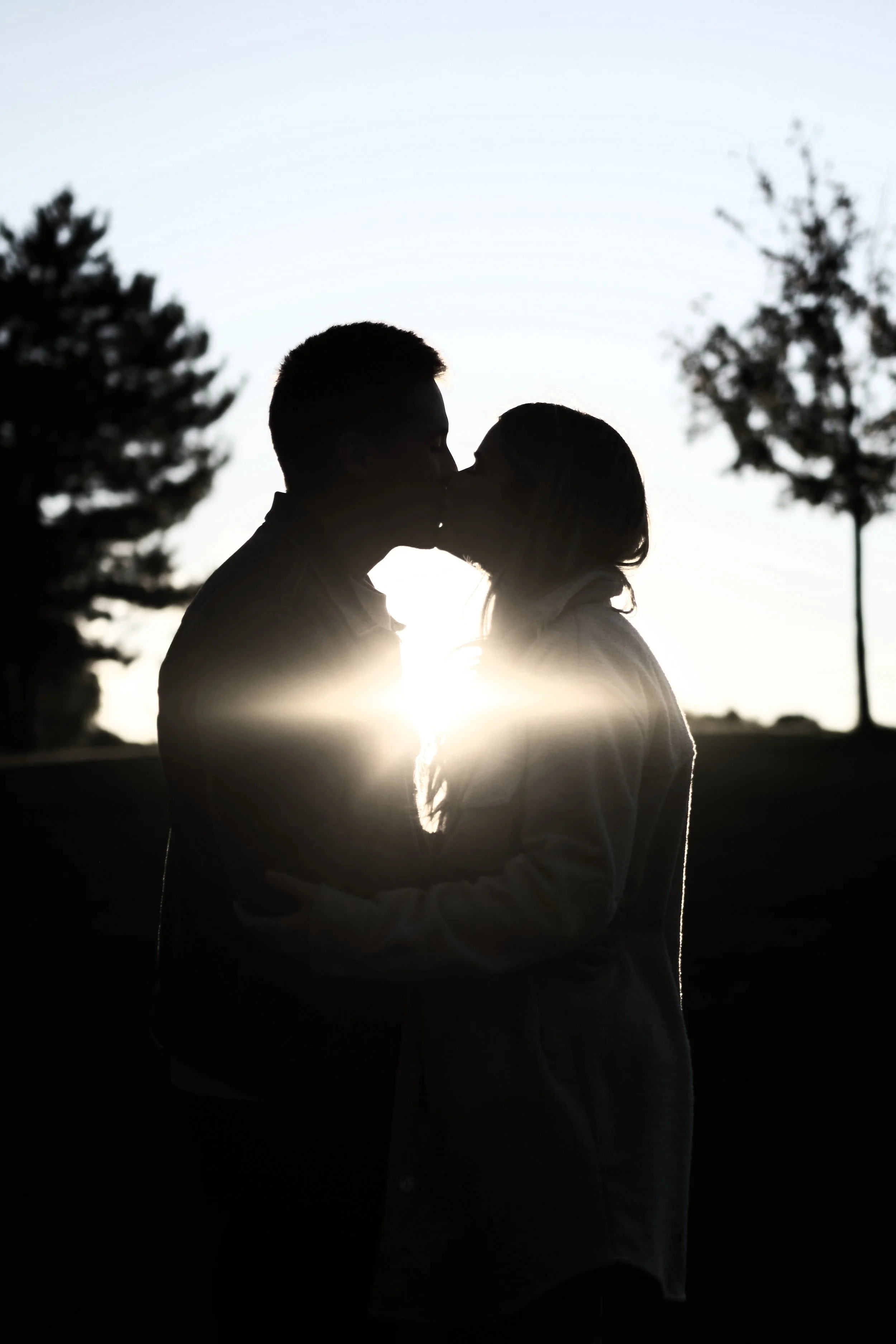 Silhouette of a couple kissing at sunset with trees in the background.