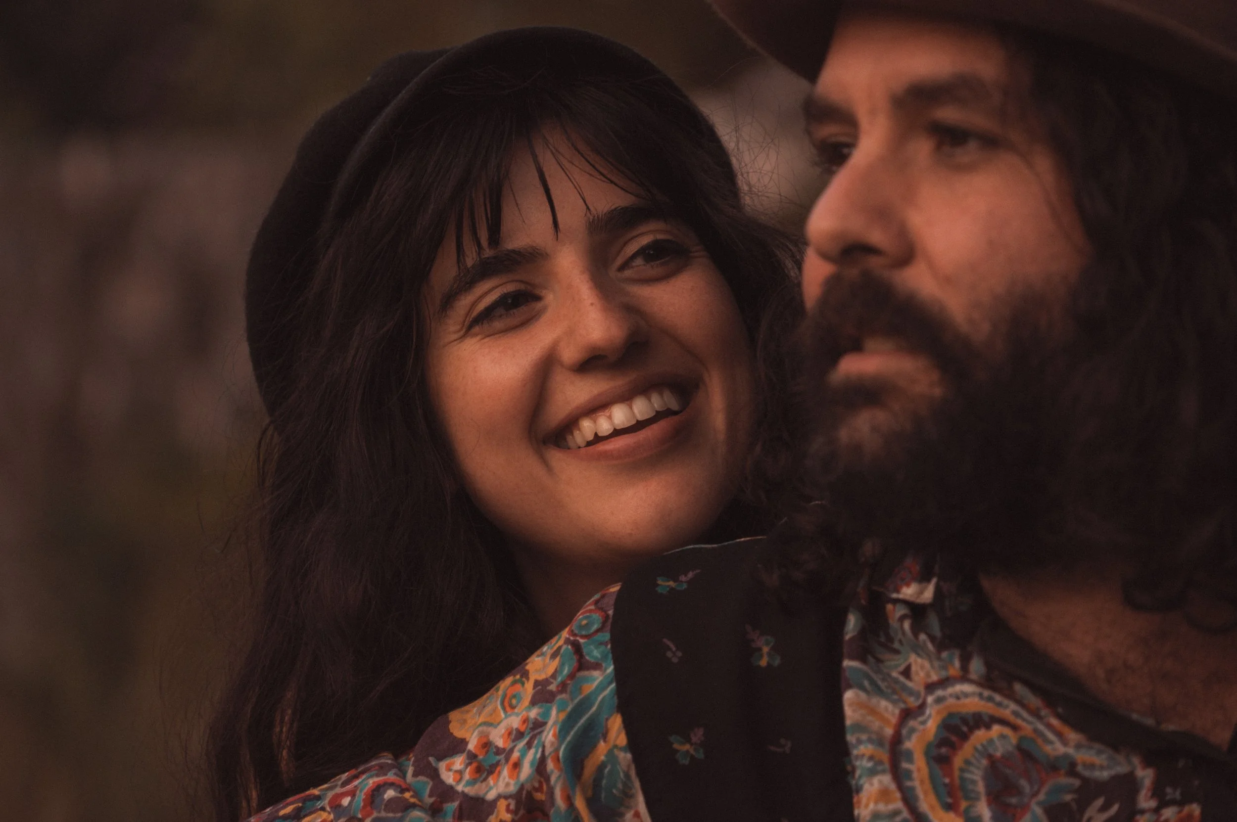 Woman smiling next to a bearded man, both wearing colorful clothing and hats.