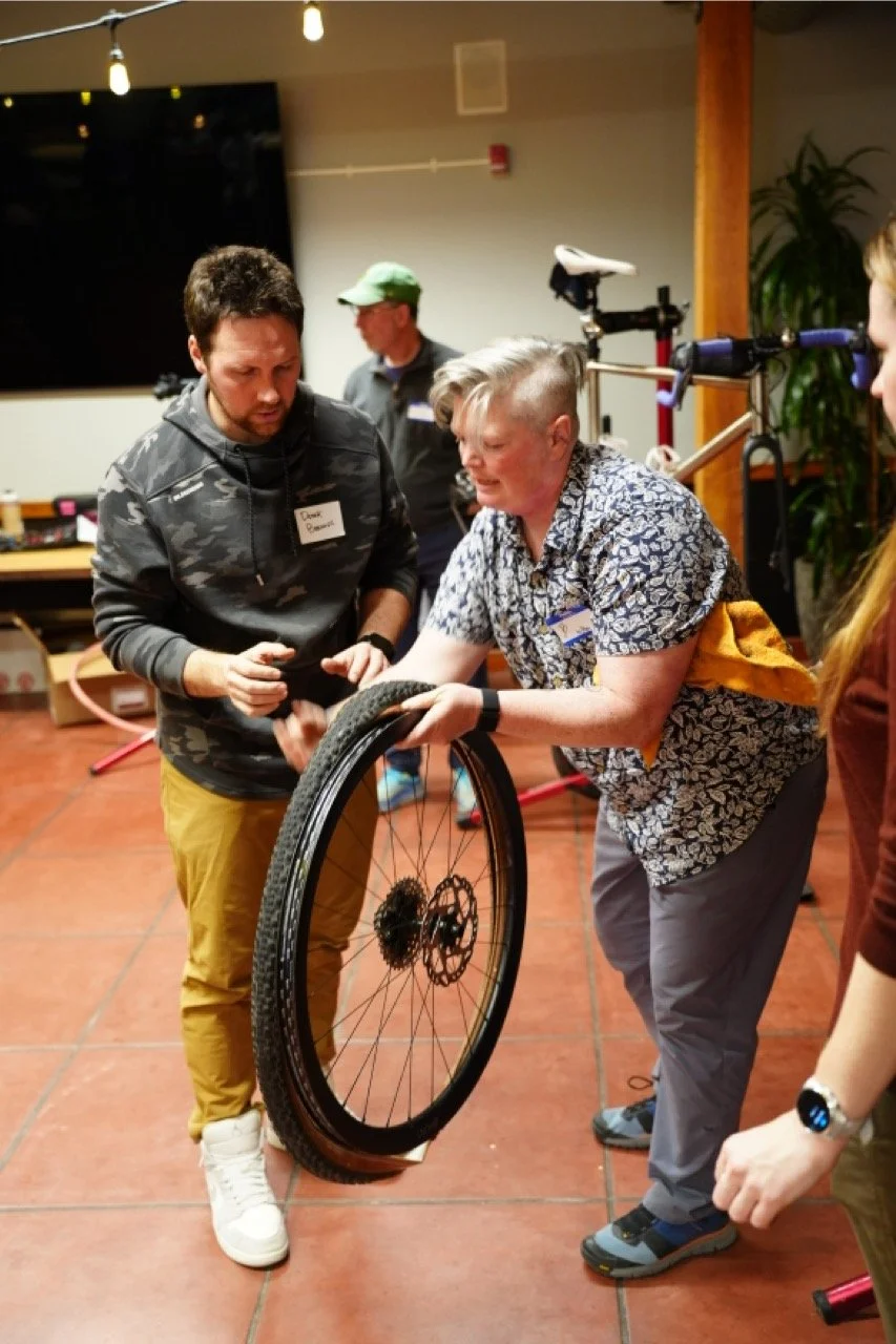 Group of people assembling or repairing a bicycle in an indoor setting.