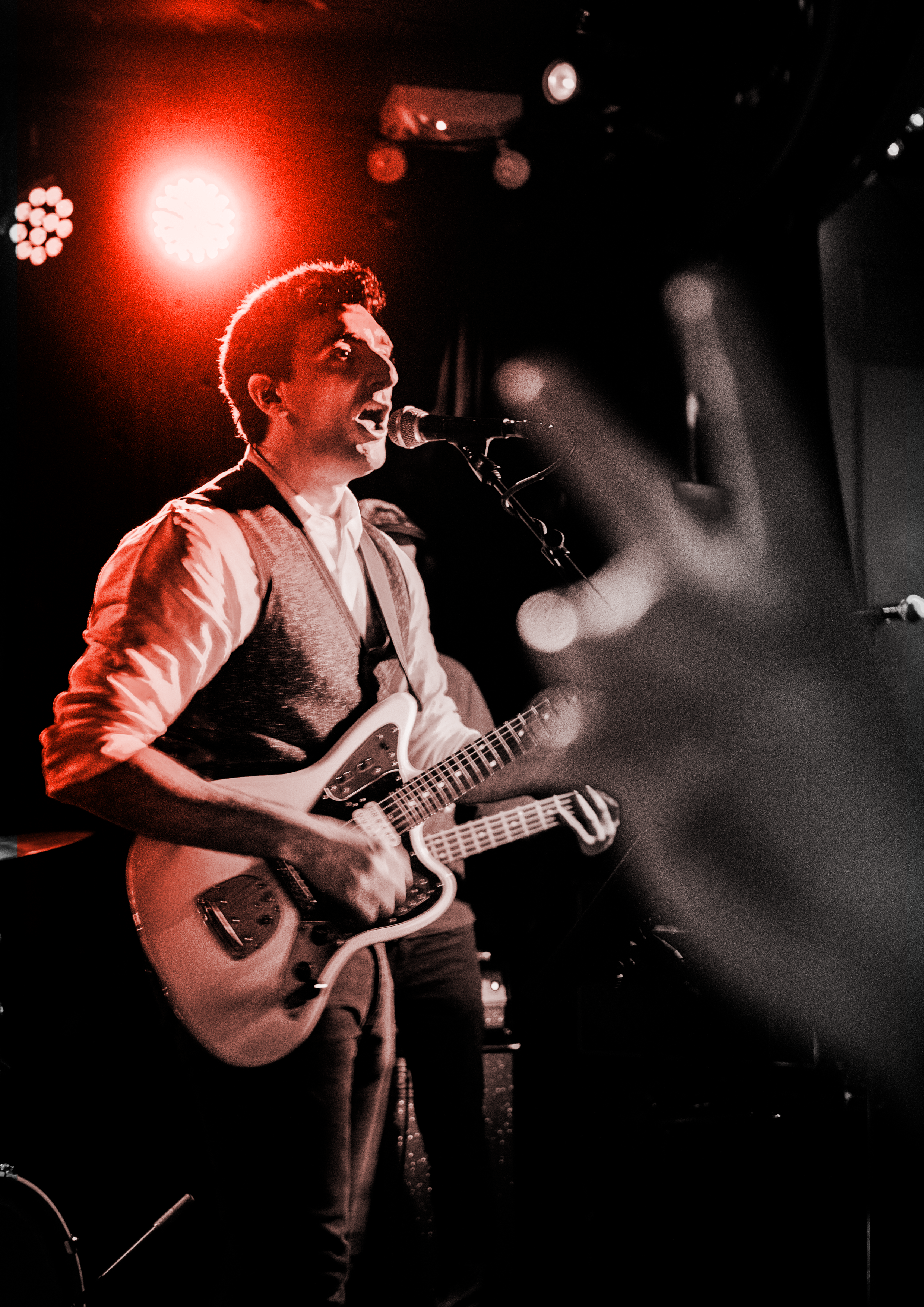Nouhi's Nomad live on stage with electric guitar and microphone under red stage lights