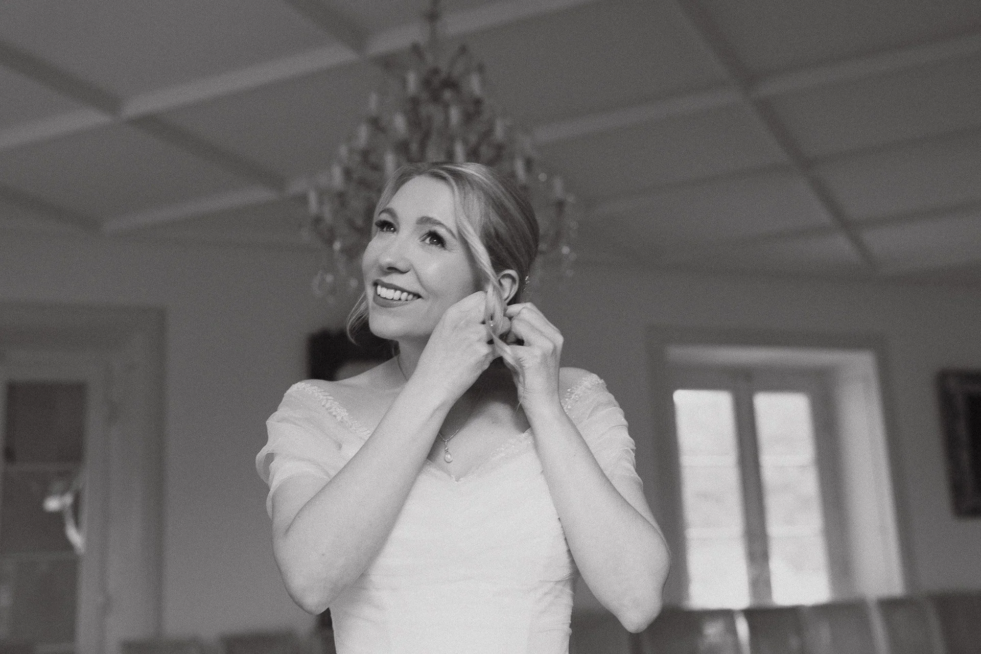 Schwarzweißaufnahme der Braut beim Anlegen ihres Schmucks während des Getting Ready.
