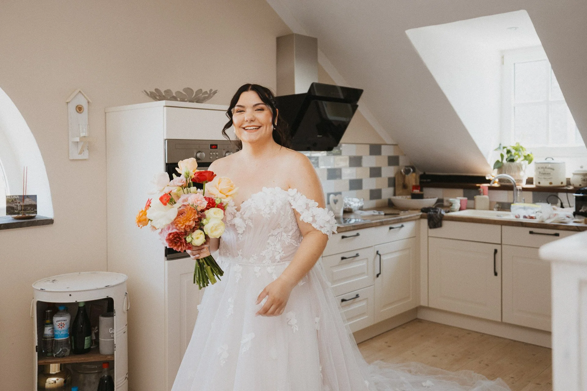 Braut mit Brautstrauß in der Küche während der Hochzeitsvorbereitungen.