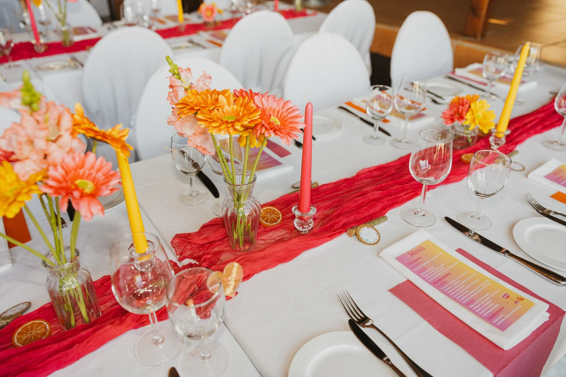 Detailaufnahme der langen Hochzeitstafel mit roten Stoffläufern und Blumen.