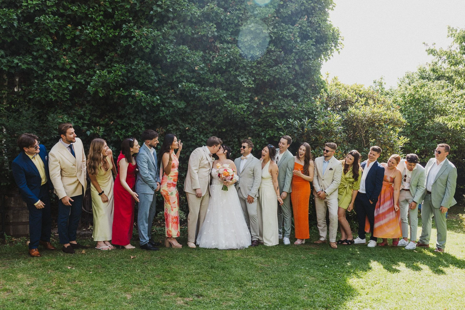 Großes Gruppenfoto mit Freunden und Trauzeugen des Brautpaars im Garten der Hochzeitslocation als lebendiger Moment der Hochzeitsreportage
