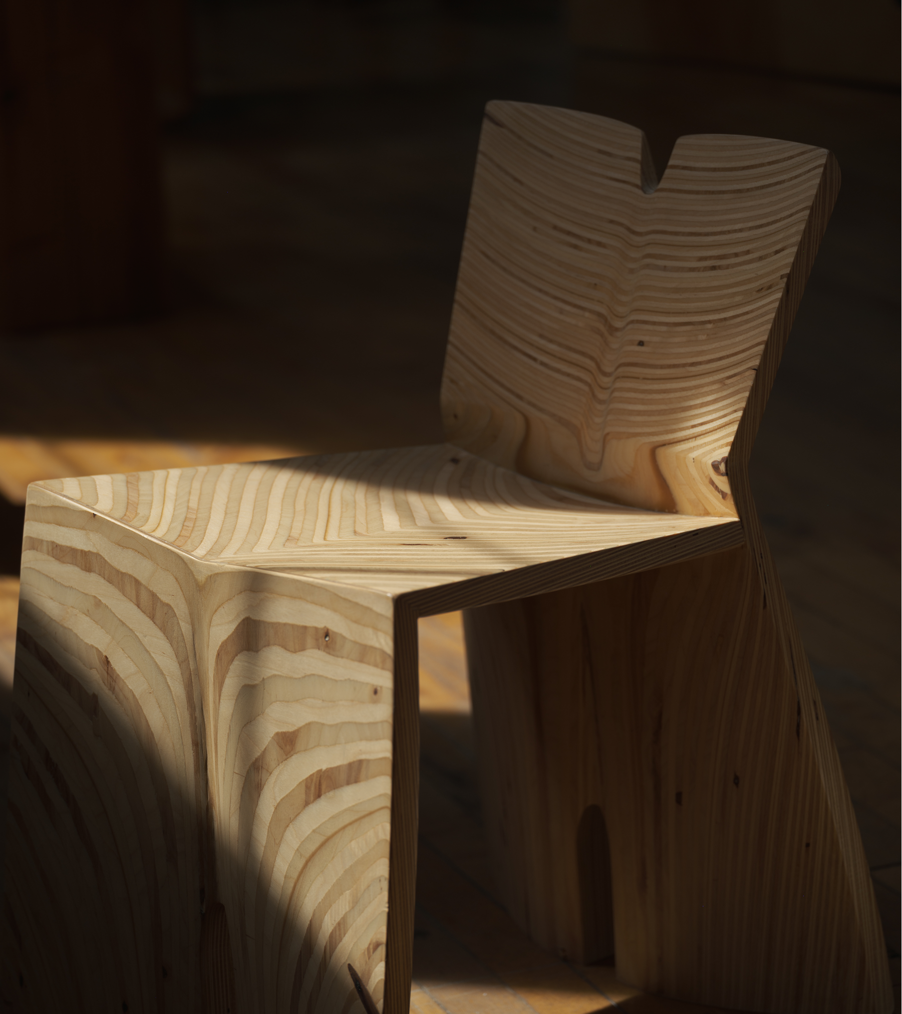 A modern wooden chair with a minimalist design, made from layered, curved wood pieces, placed on a wooden floor.