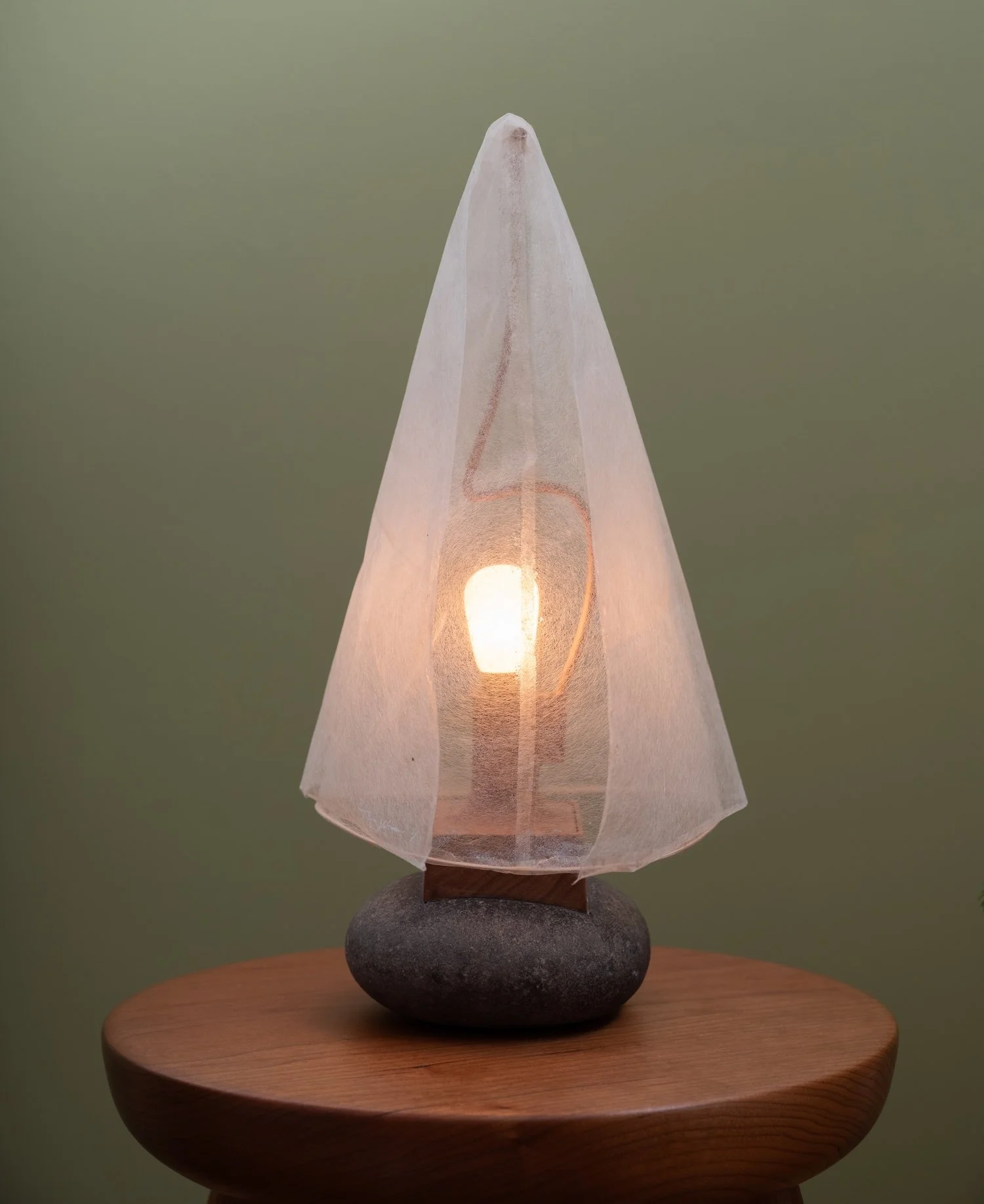 Decorative table lamp with a stone base, fabric cover, and exposed light bulb, placed on a wooden surface.