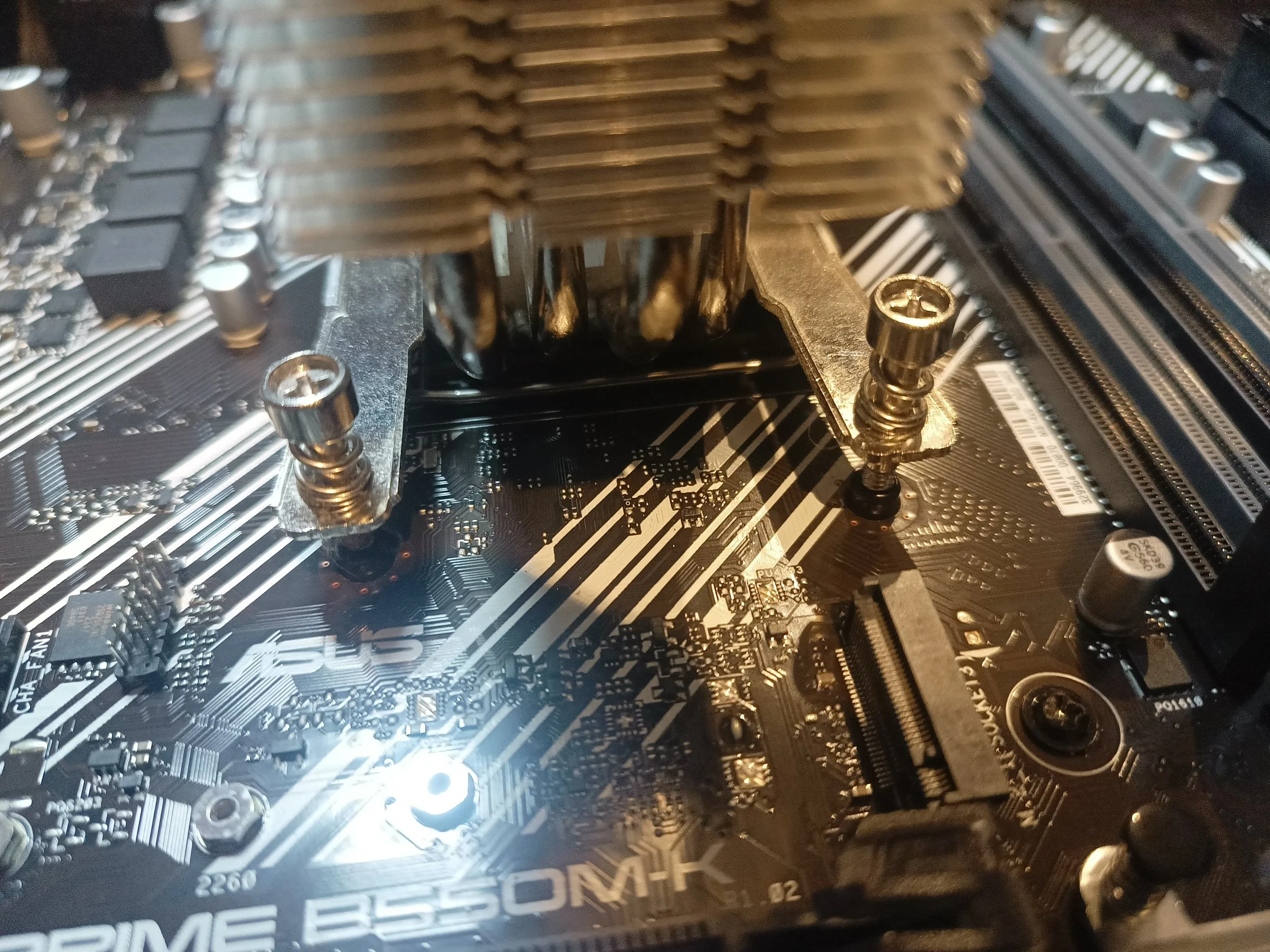 Close-up of a computer motherboard with a large heatsink and multiple metal screws.