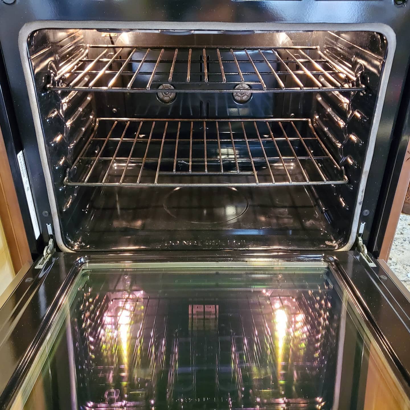 An open stainless steel oven with two racks inside and a glass door reflecting the kitchen surroundings.
