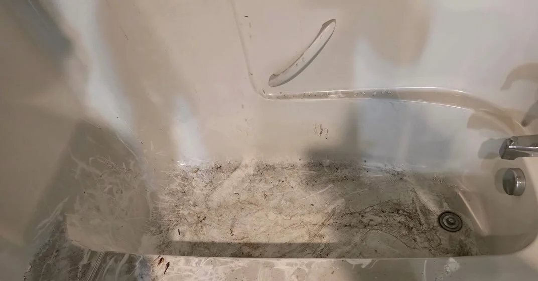 Dirty bathtub with black mold, soap scum, and dirt along the bottom and sides.