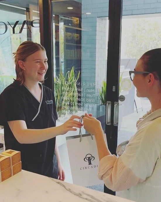 A person wearing dark clothing handing a shopping bag labeled "Circadia" to another person at a store counter of Utopia Skin and Spa.