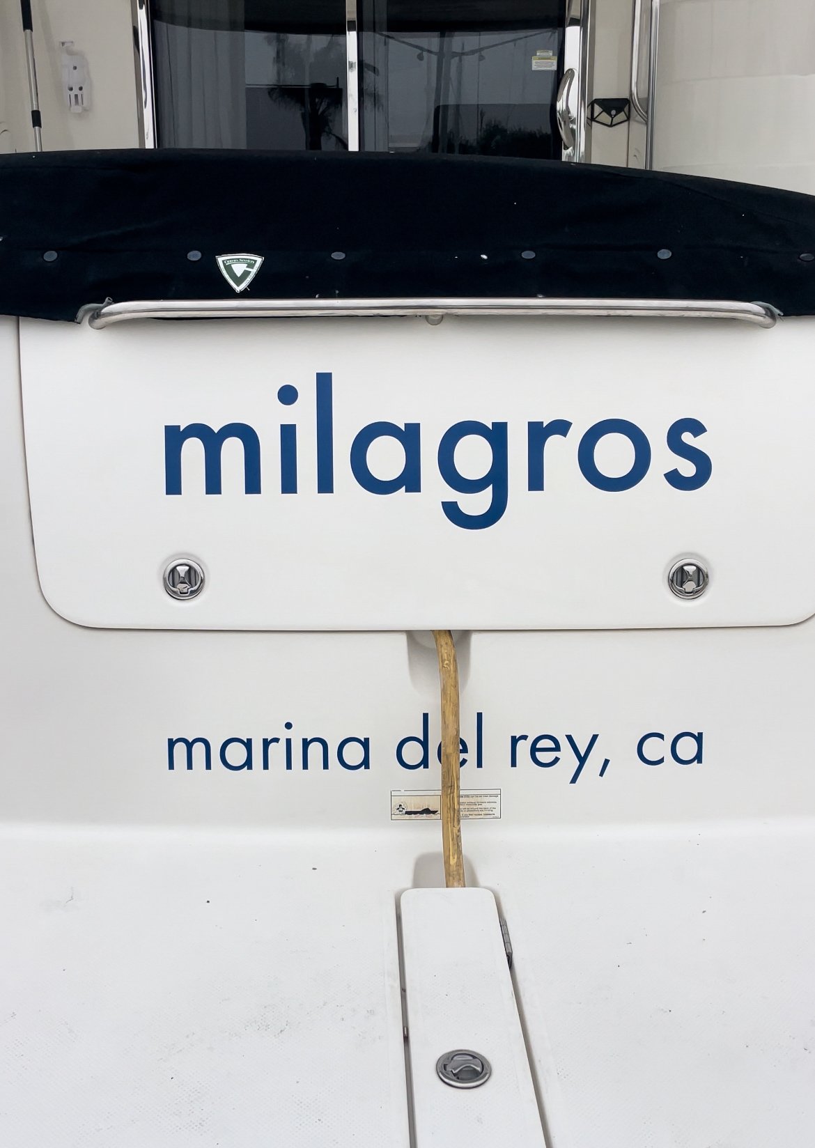 Rear view of a boat named 'milagros' docked at Marina del Rey, California. The boat has a black cover and visible rope.