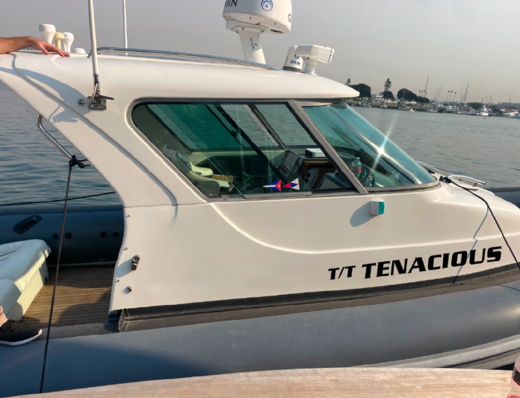 Side view of a white motorboat named 'T/T Tenacious' docked in a marina, with visible radar and antenna on the roof.