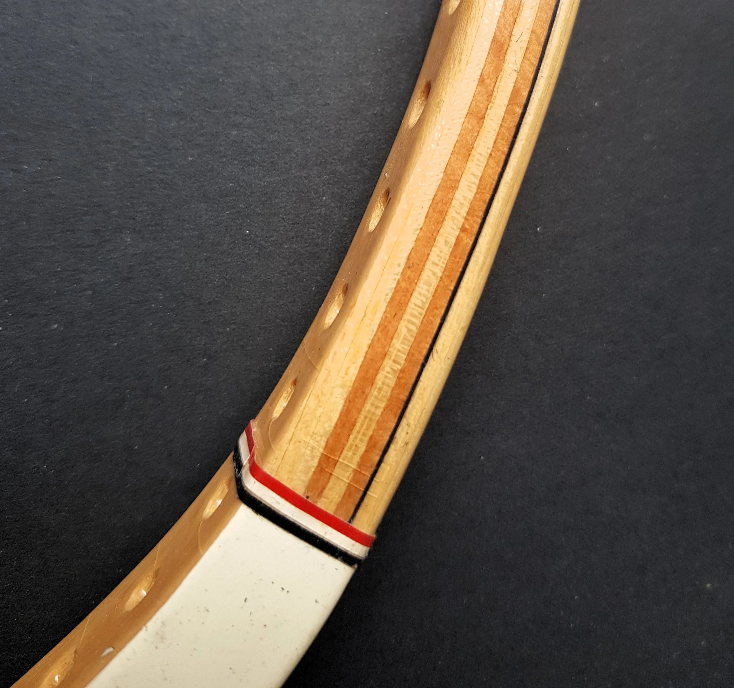Close-up of a wood tennis racket frame showing timbers and with stringing holes on a dark background.