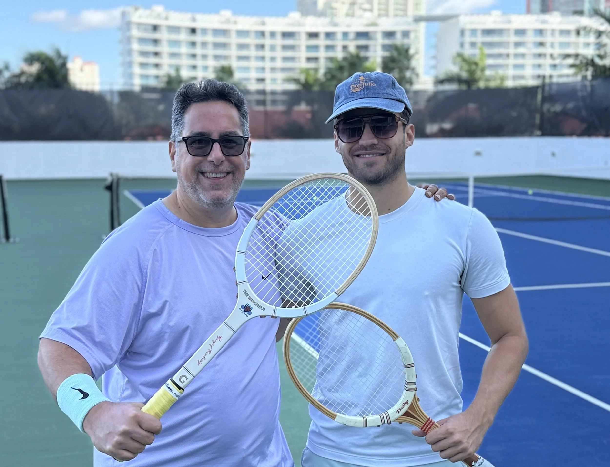 Two players together on a court holding wood tennis rackets.