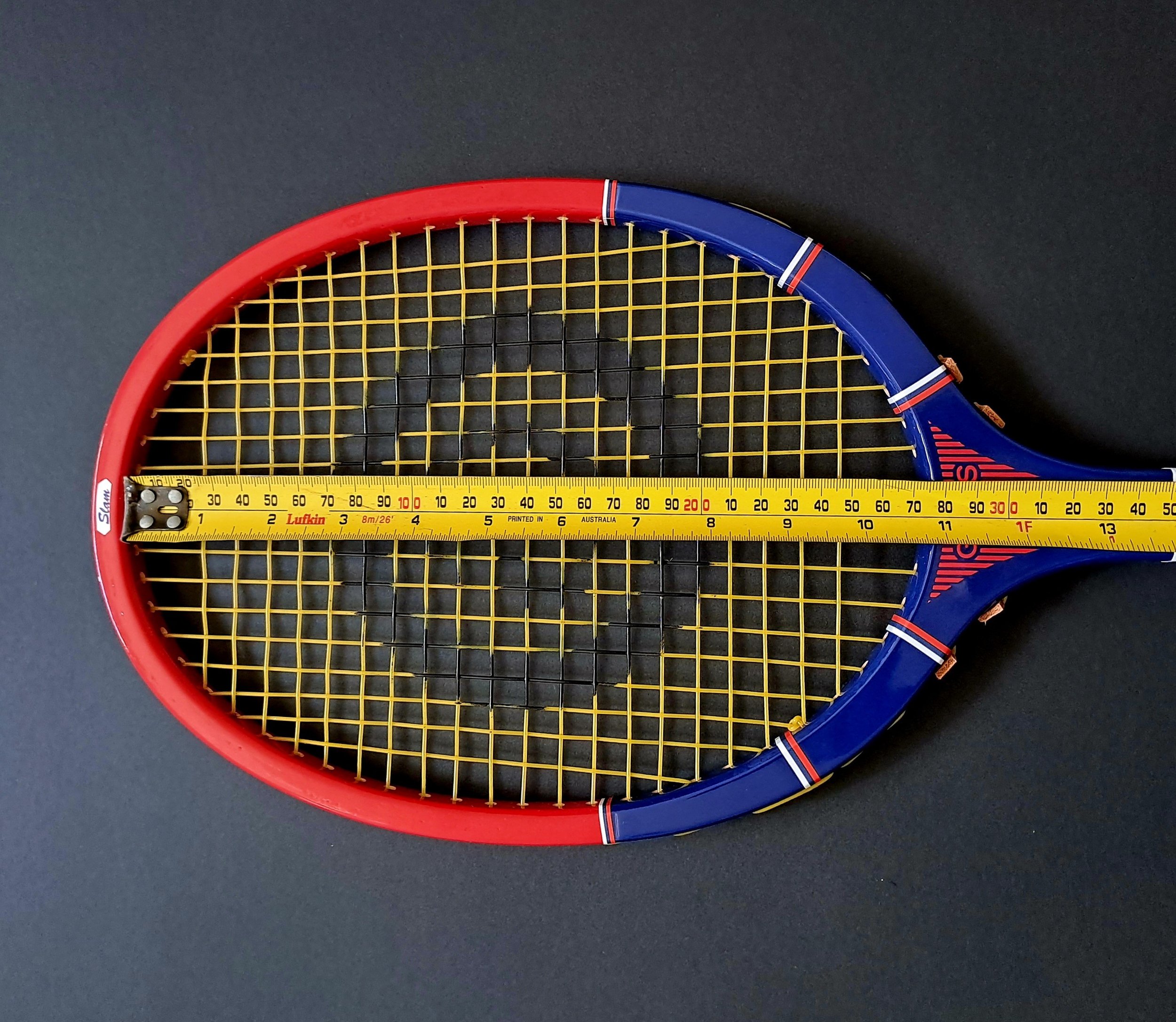 Head of a Grays racket with tape measure on a black background.