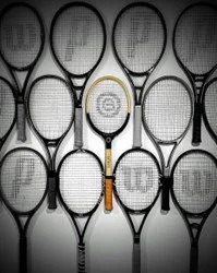 A collection of black and gray tennis rackets displayed on a wall, with one wooden racket in the centre.