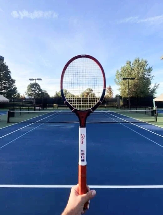 A hand holding a Grays racket on a blue court.