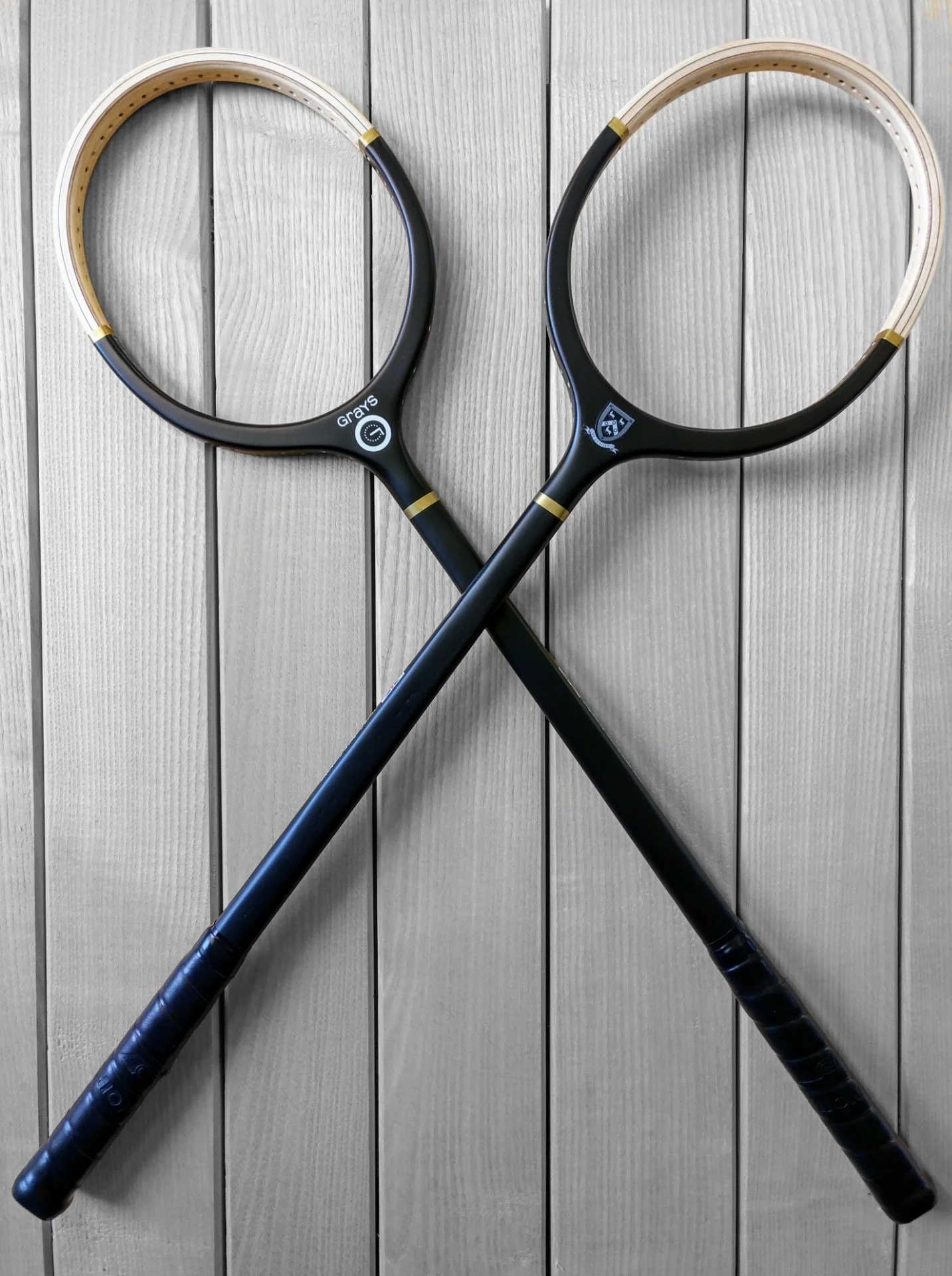 Two crossed Grays rackets against a timber background.