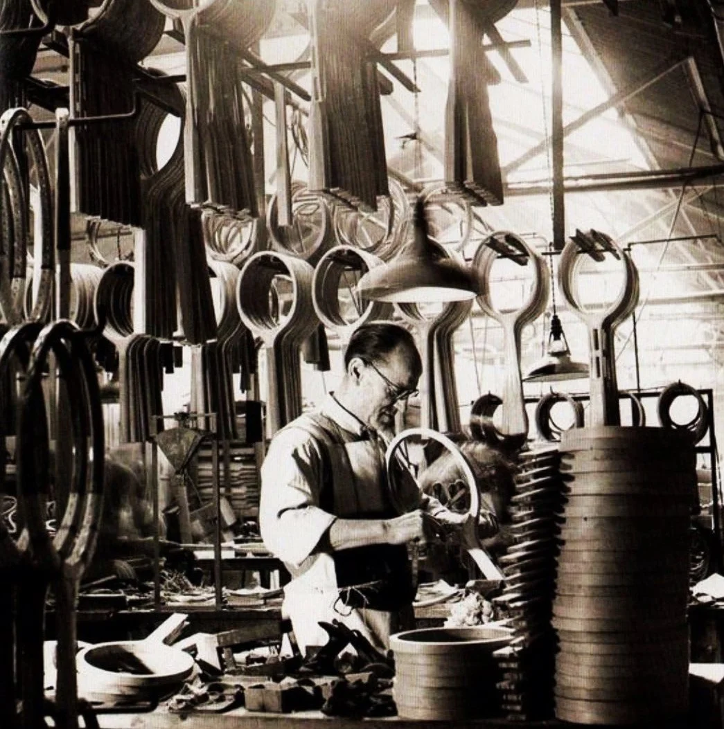 Man working in a factory, surrounded by wood tennis frames and equipment. Black and white photo.