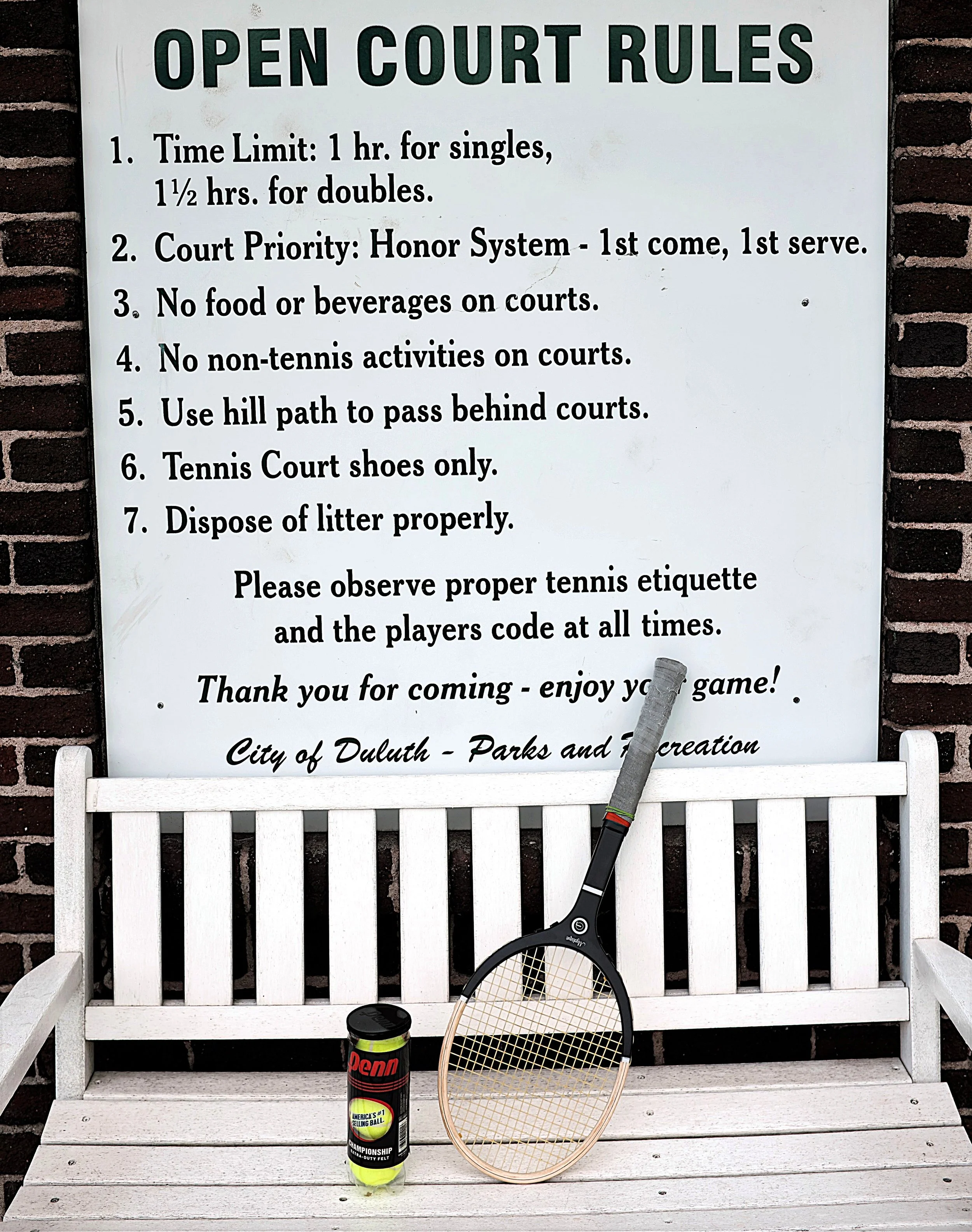 Grays Mystique on a sitting bench next to a can of tennis balls in front of a sign stating club rules.