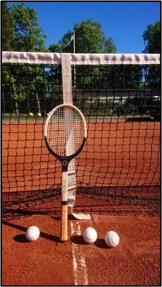 Grays Masterpiece tennis racket and white balls on a clay court near the net.