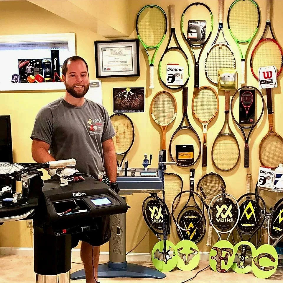 man next to stringing machine with rackets in background