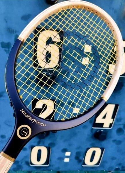 A wood tennis racket with a blue frame labelled 'Masterpiece' in front of a tennis scoreboard showing game scores..