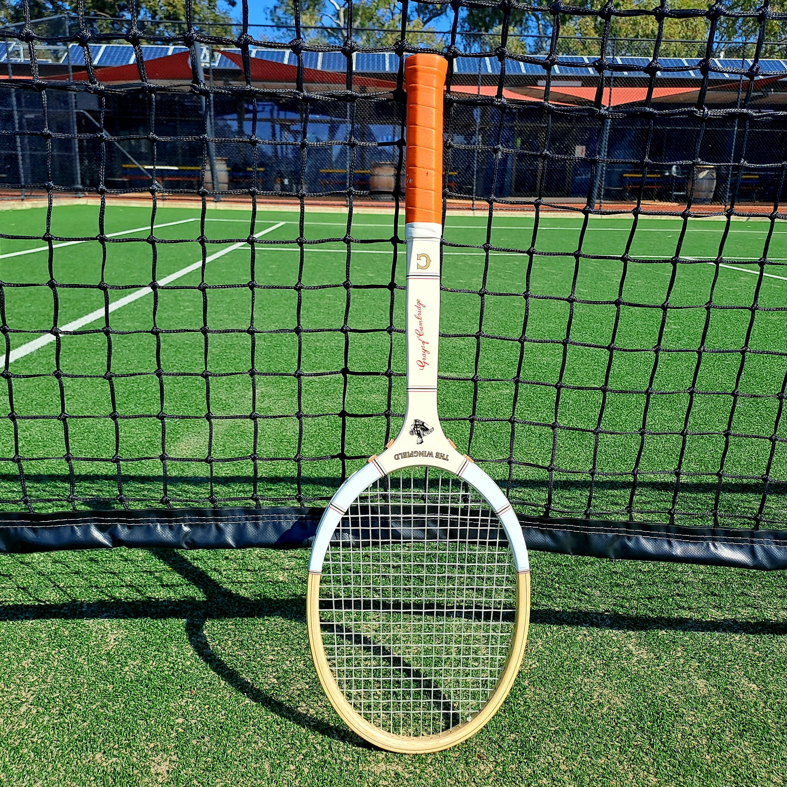 Grays The Wingfield against a net on a grass court with clubhouse in background.