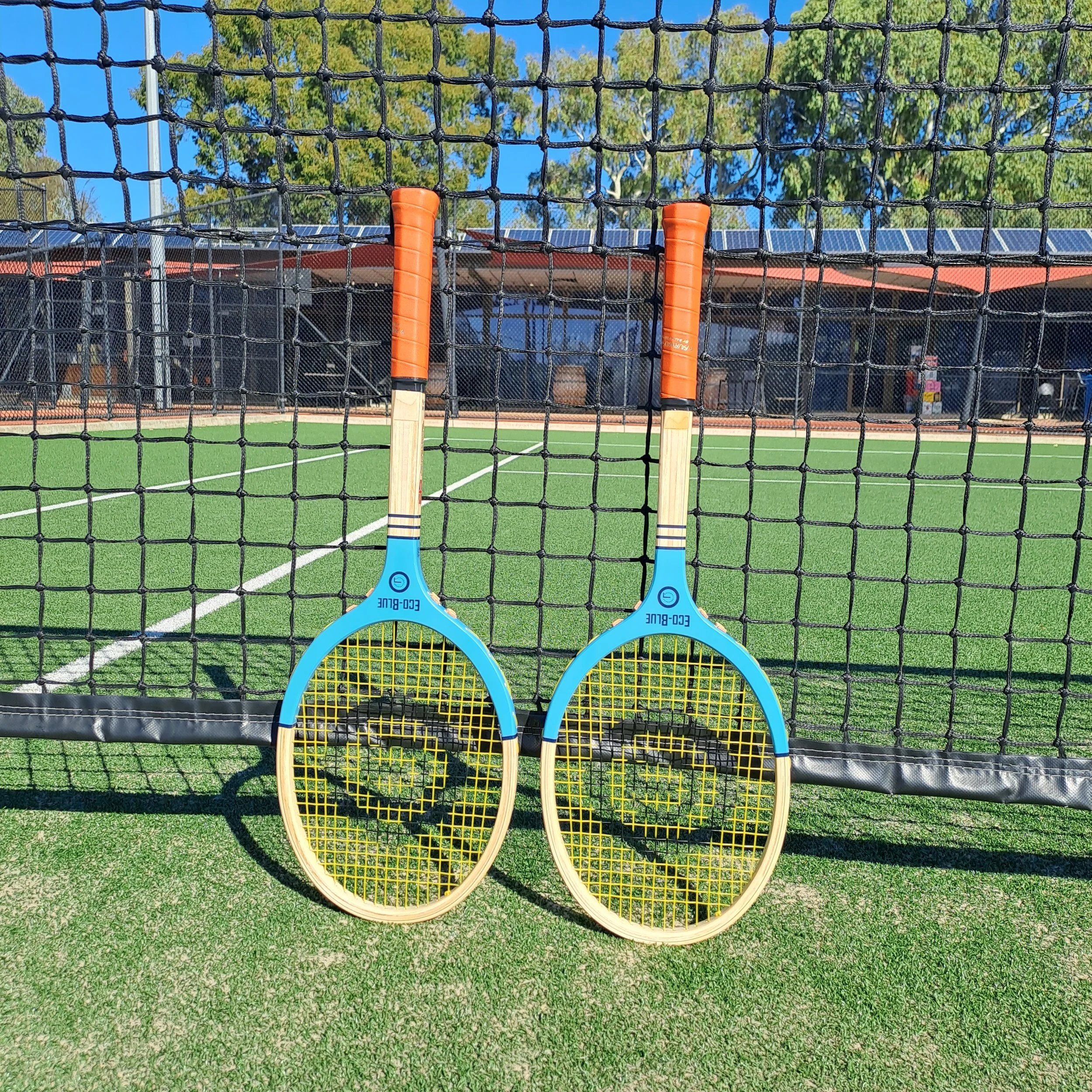 two Grays rackets leaning against a net on a tennis court.
