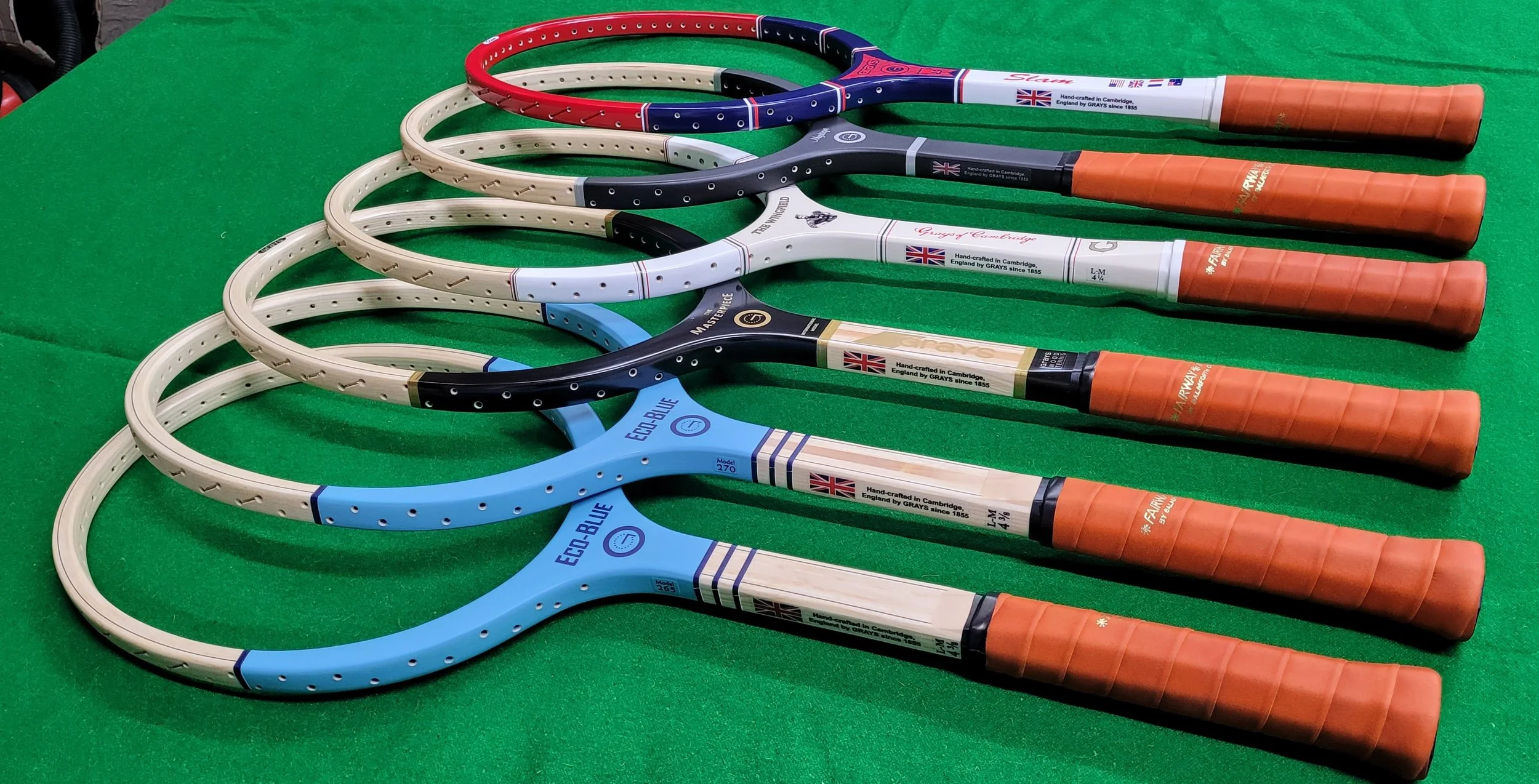 Six new wood tennis frames laying on green surface