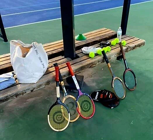 A bunch of wood rackets and tennis gear on courtside seating.
