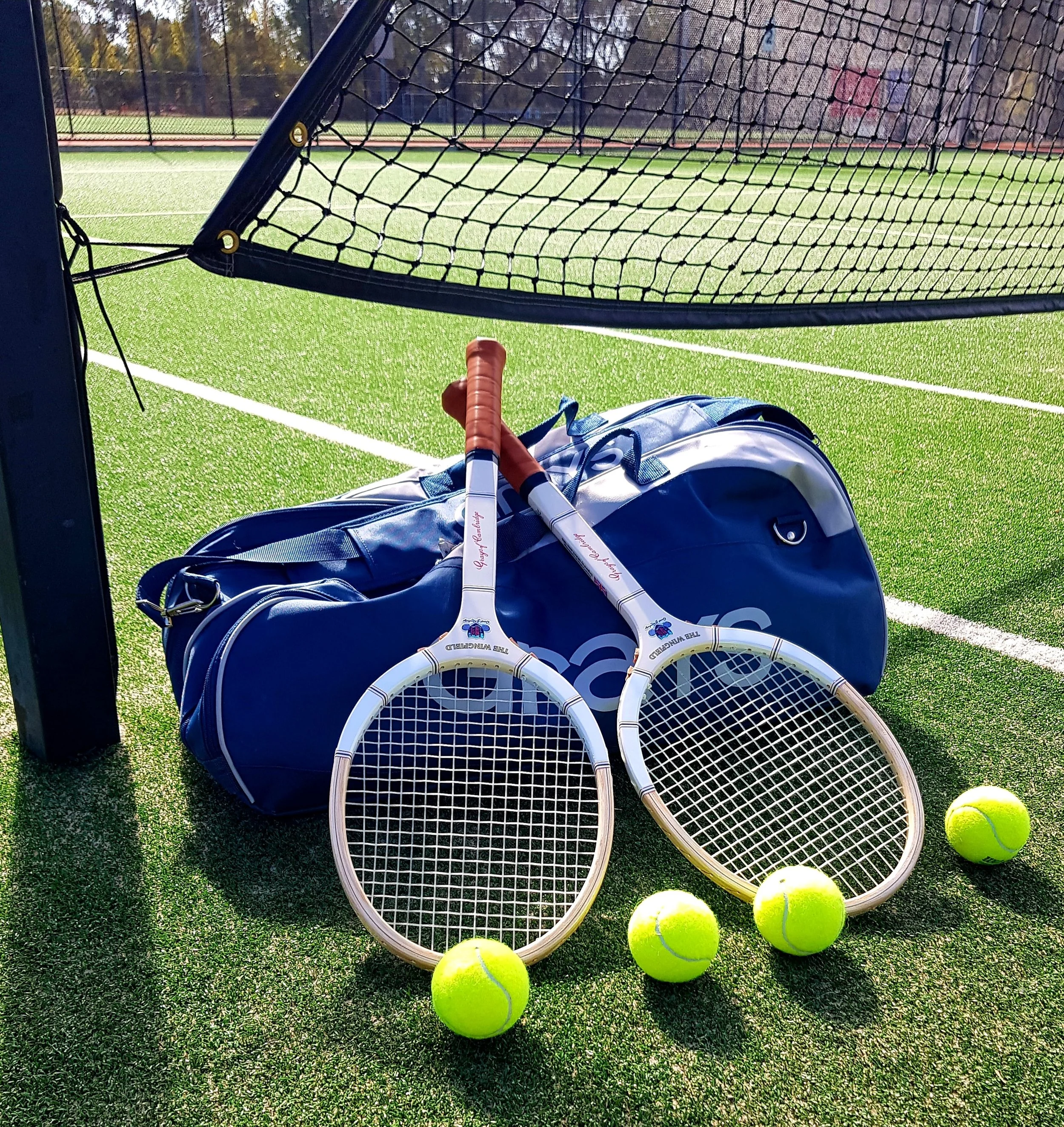 Two Grays rackets resting on a Grays bag on a grass tennis court.