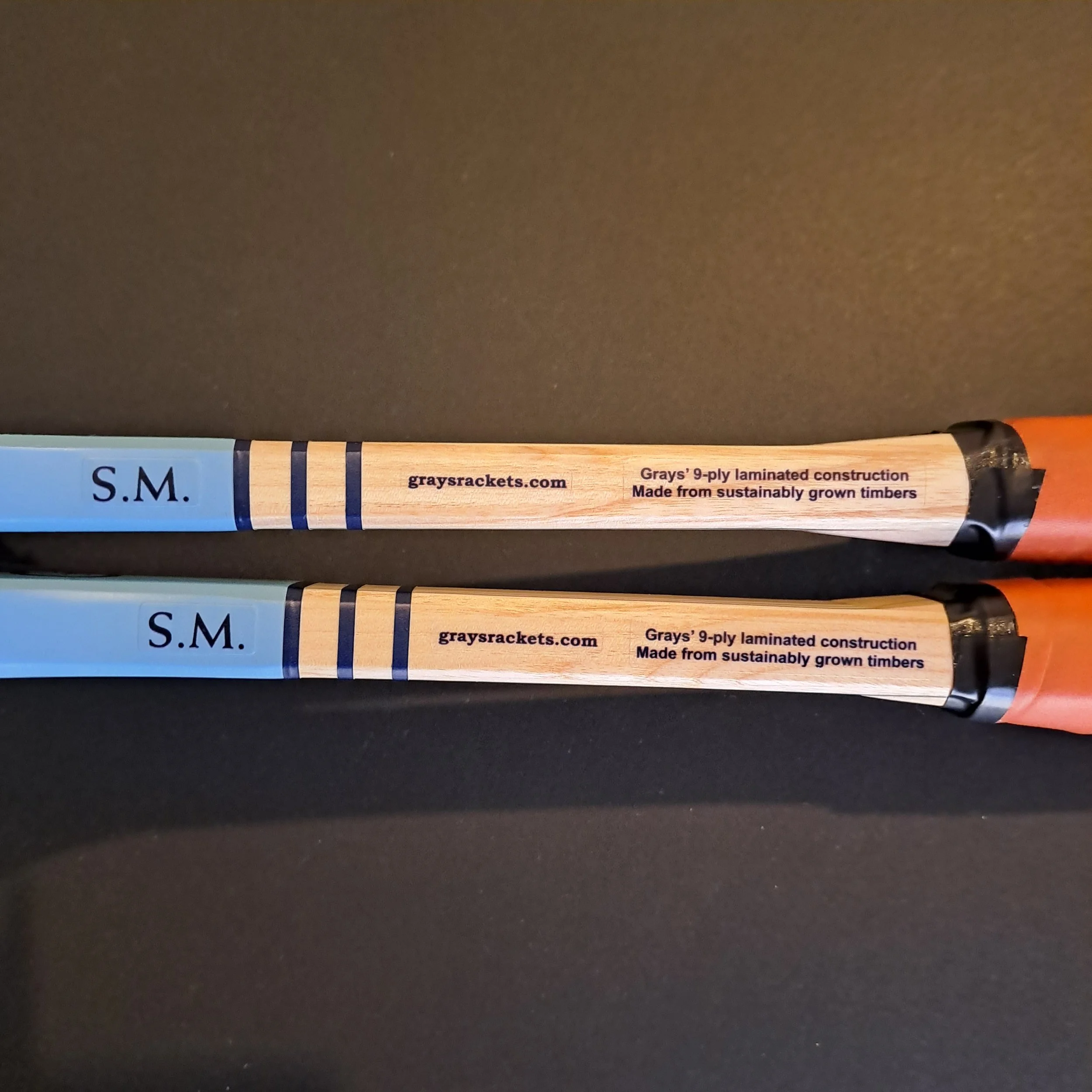 Opposite full side shaft view of two Grays Eco-Blue rackets against a black background