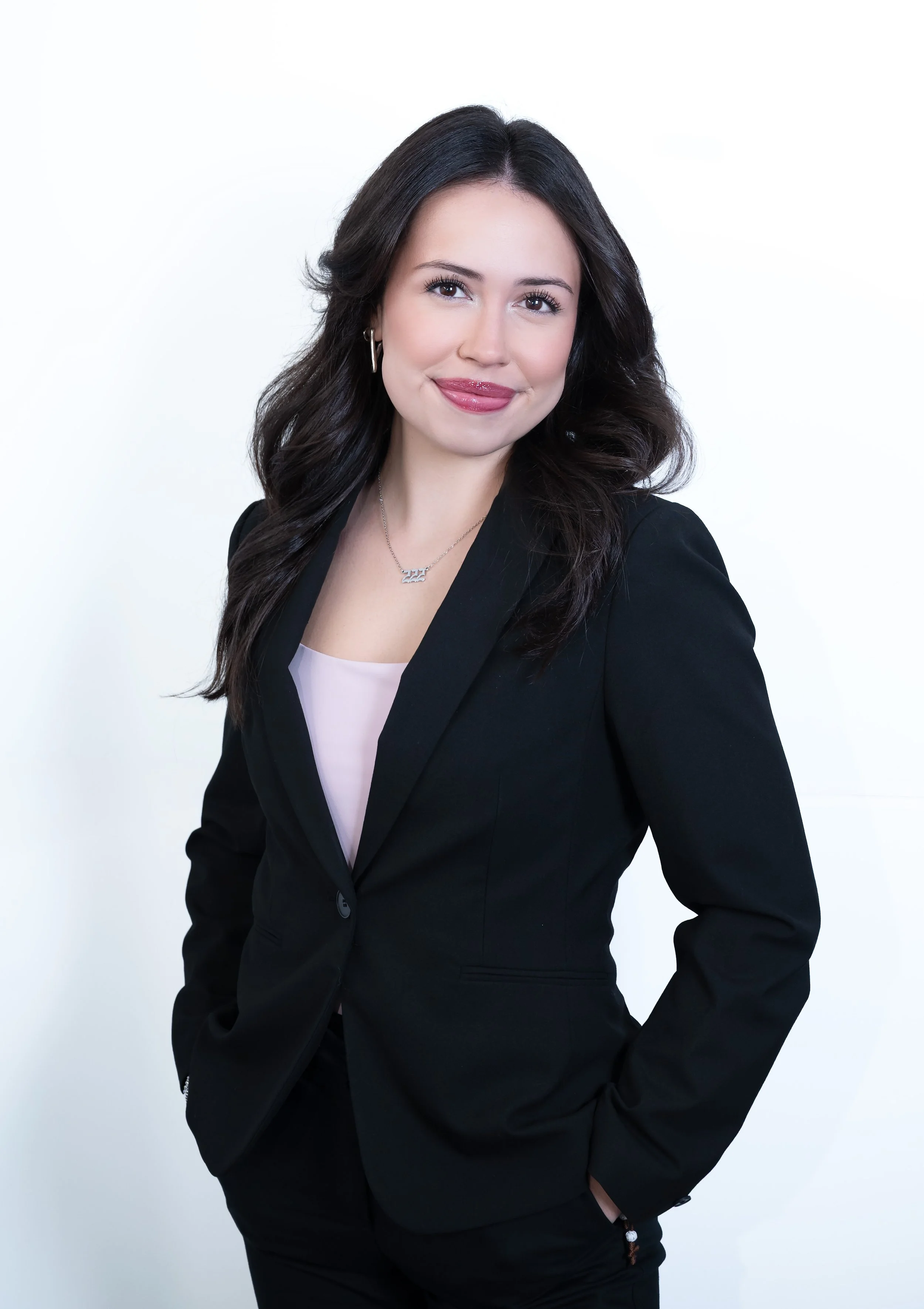 “Professional business headshot of a woman wearing a black blazer and light pink top, smiling against a white background.