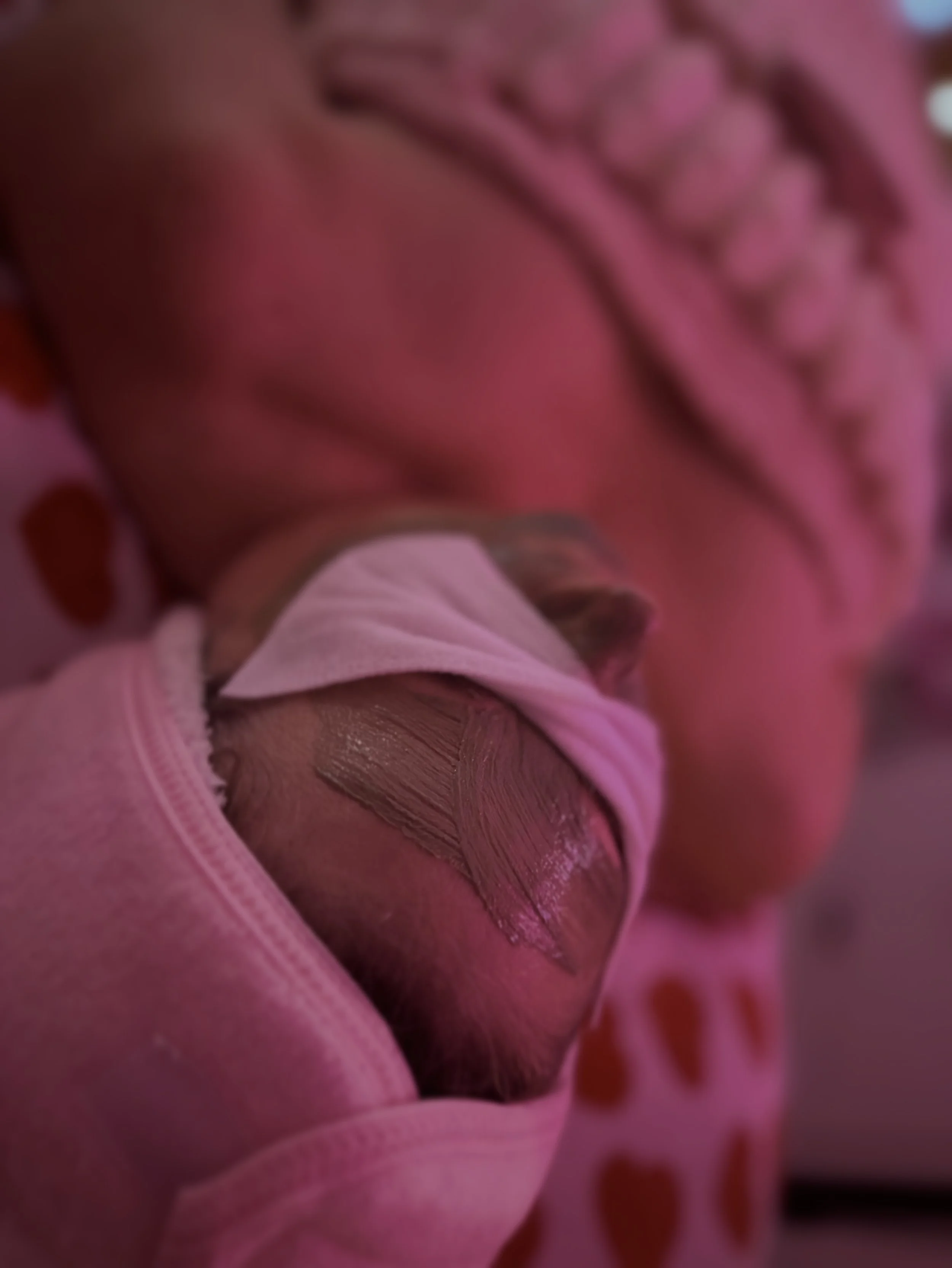 Person lying down at a spa or facial treatment, wearing eye pads and a headband, with a towel covering their chest, in a room illuminated with purple light.