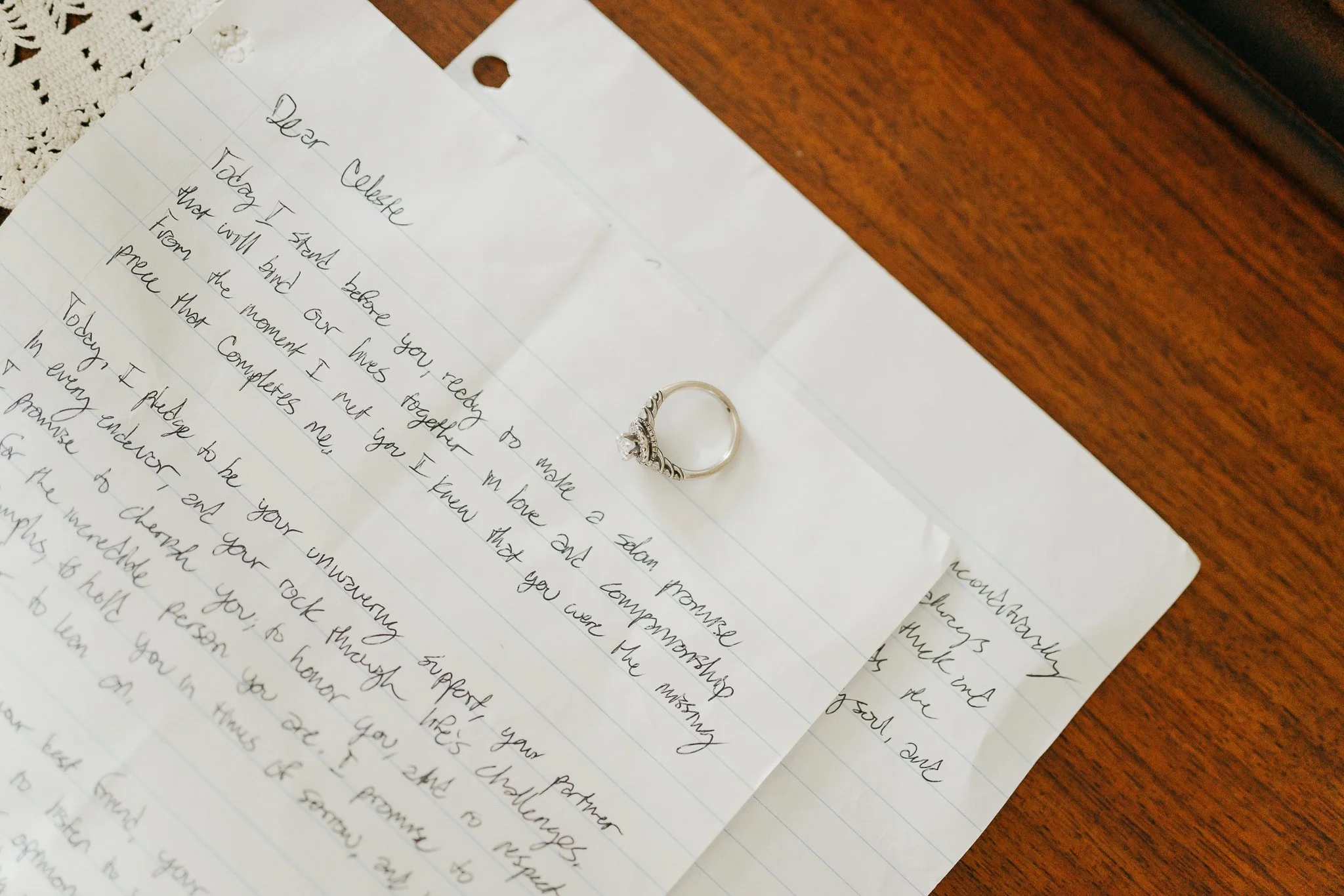 A handwritten letter on lined paper with a wedding ring placed on top, both resting on a wooden surface.