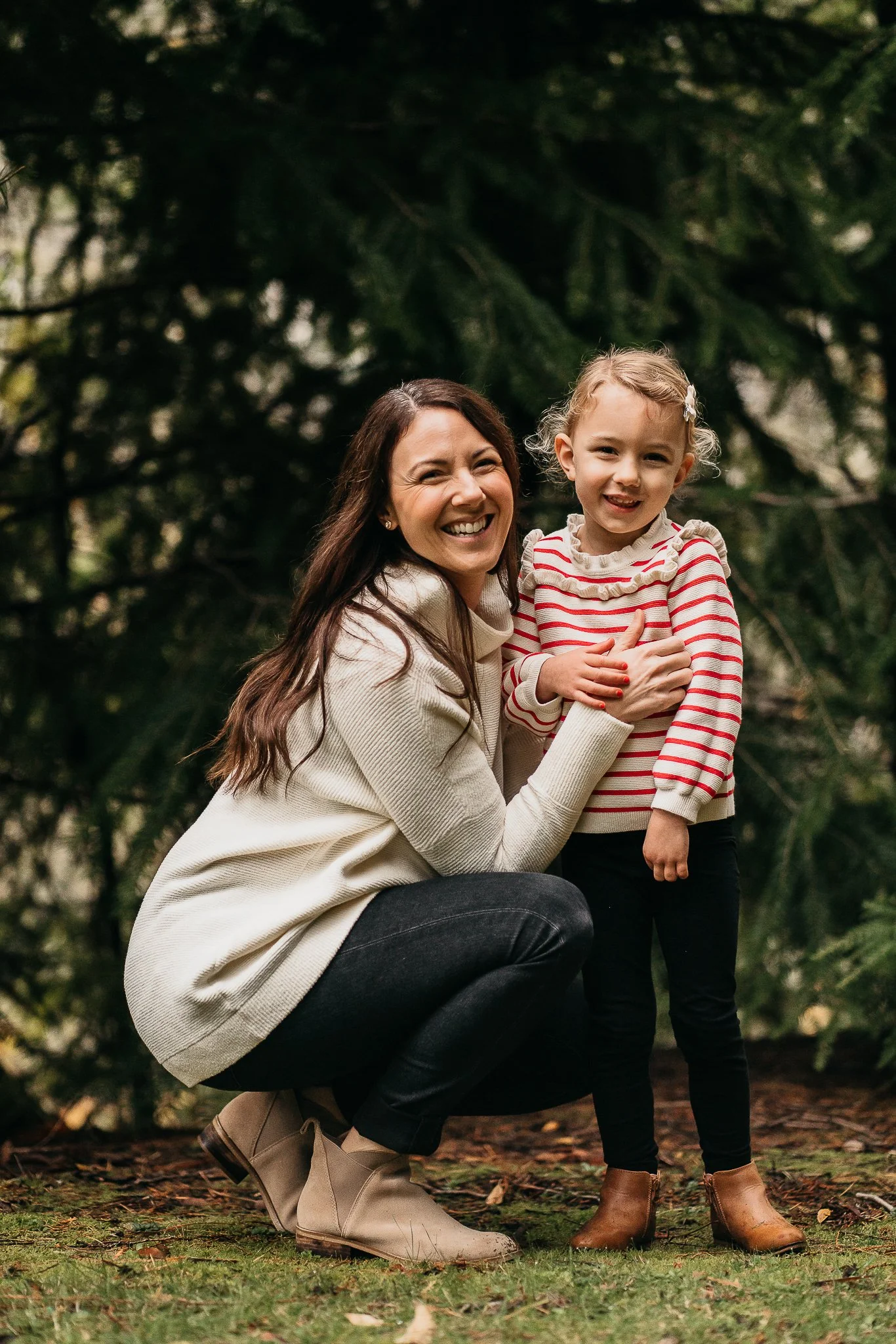 A woman and a young girl smiling outdoors, surrounded by greenery.