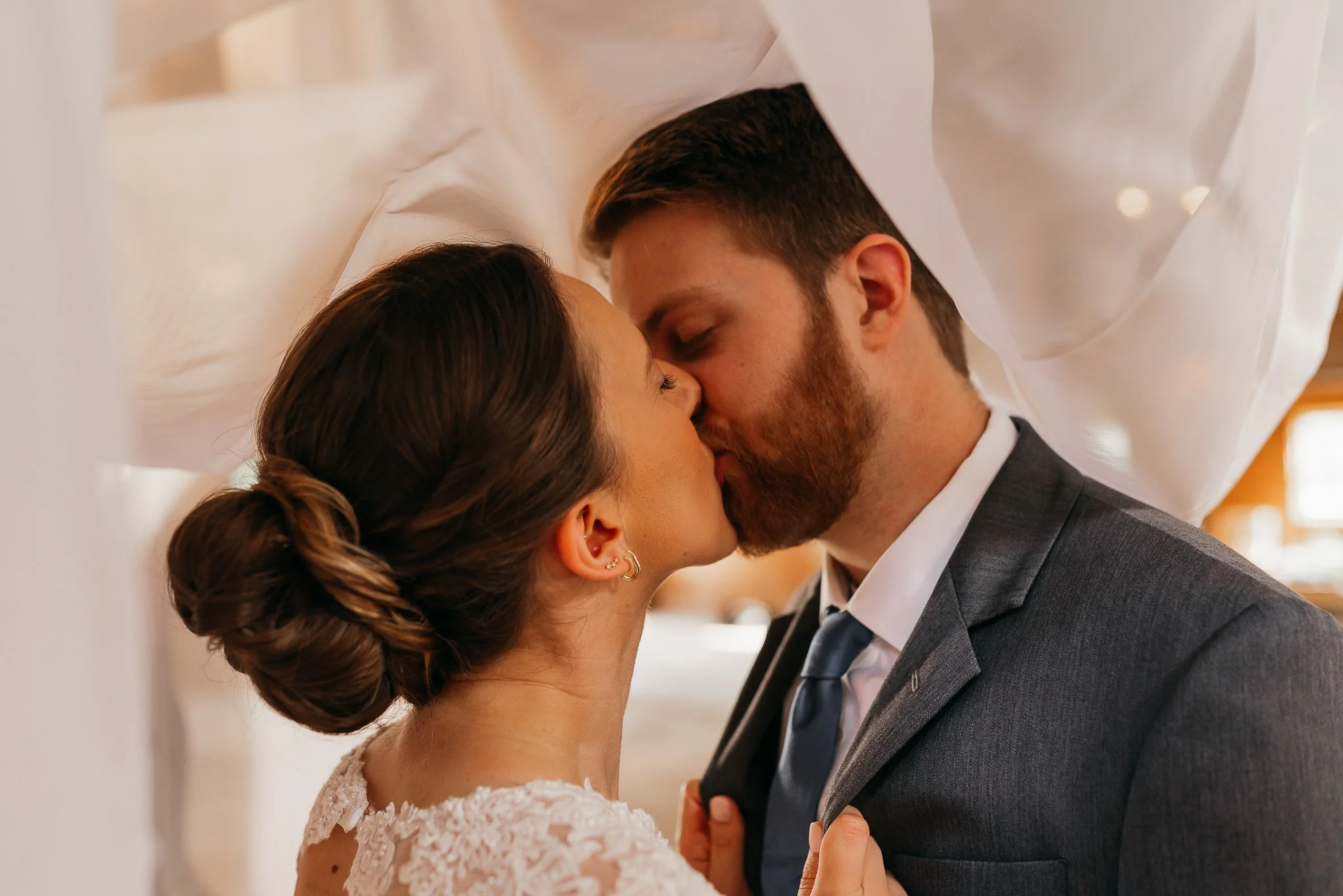 A bride and groom sharing a kiss during their wedding ceremony underneath a white fabric canopy.